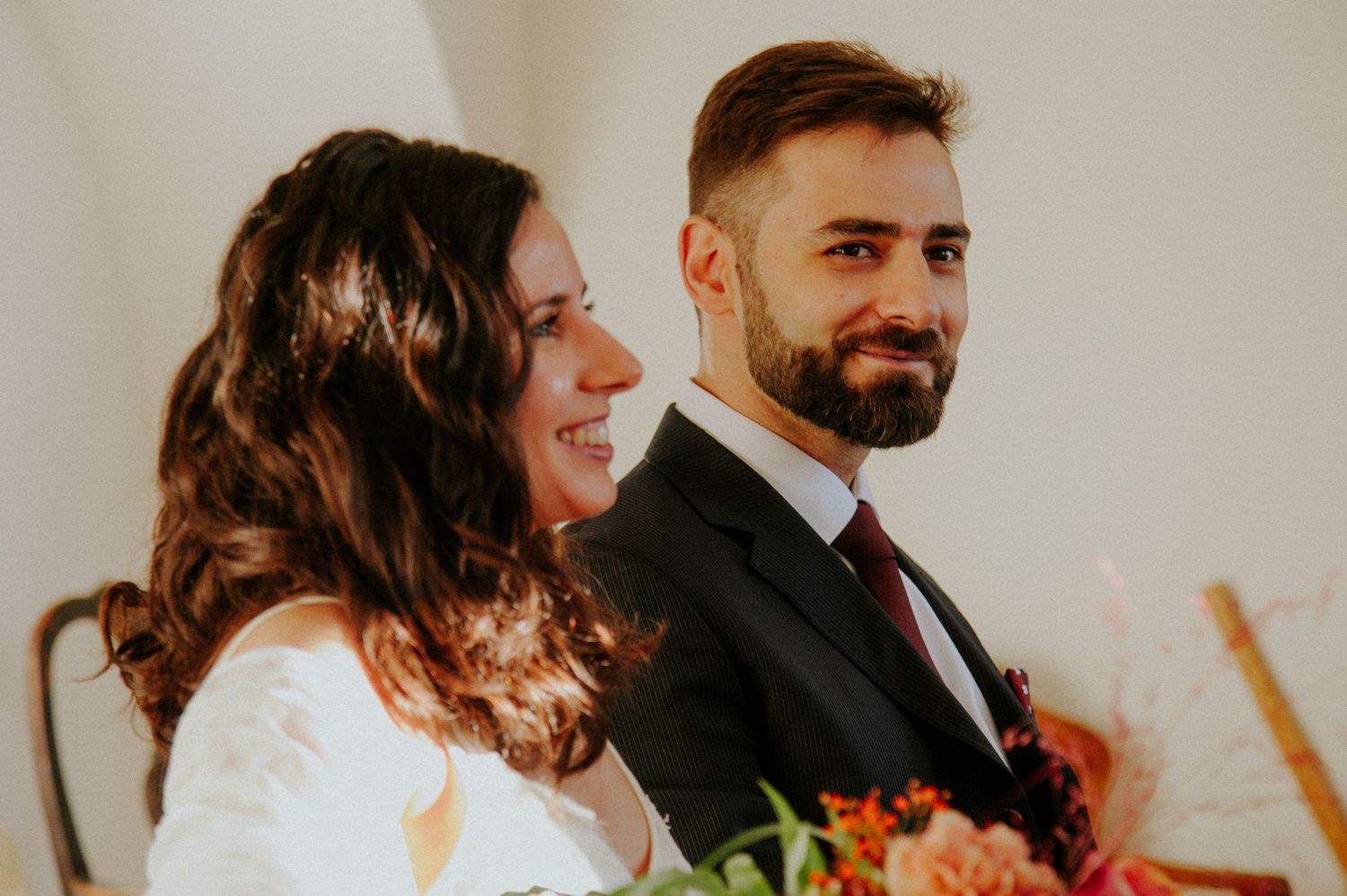 A couple shares a candid moment during their wedding ceremony, with the bride holding a colorful bouquet.