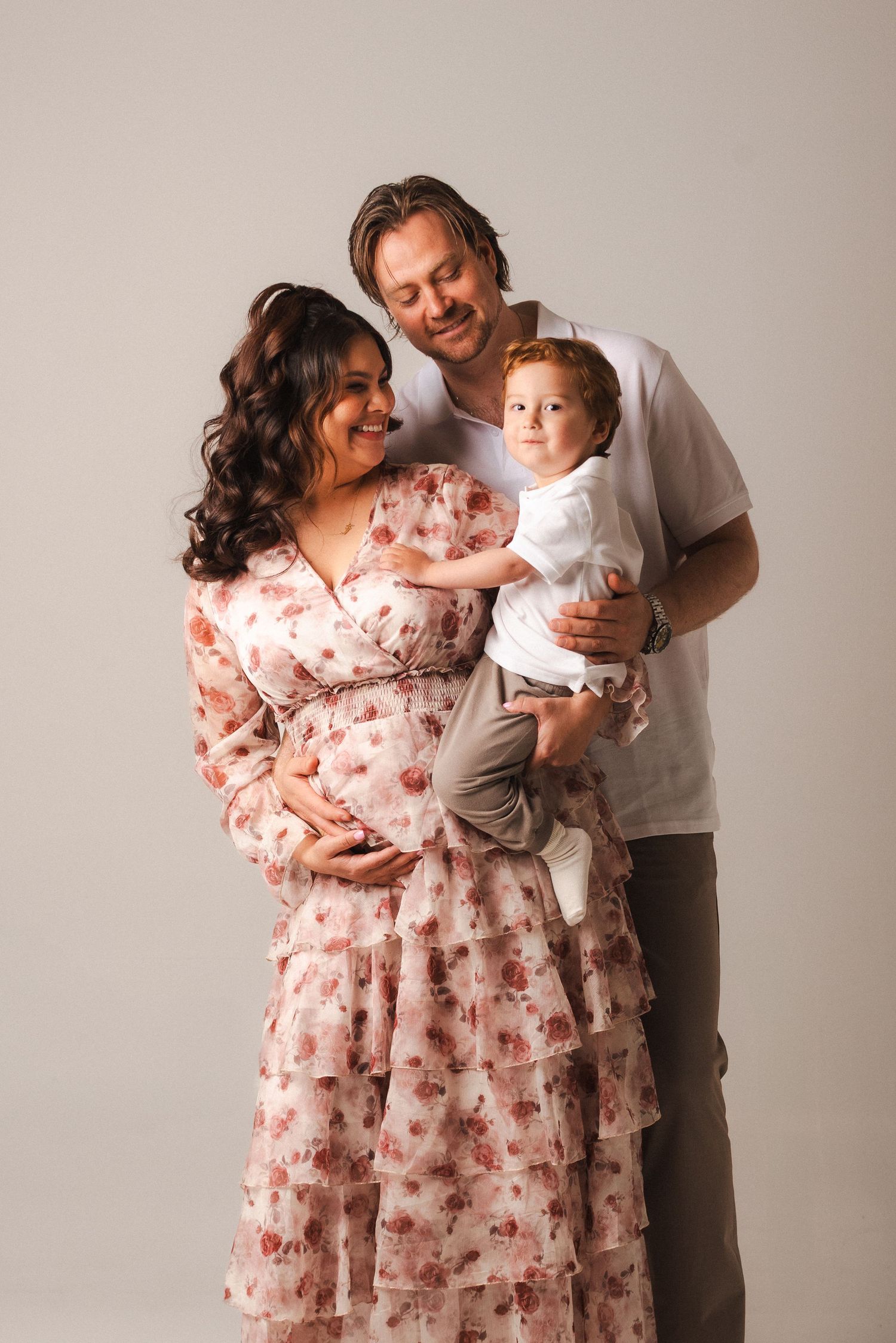 A family in casual attire shares tender moments in a studio photo series against a neutral background.