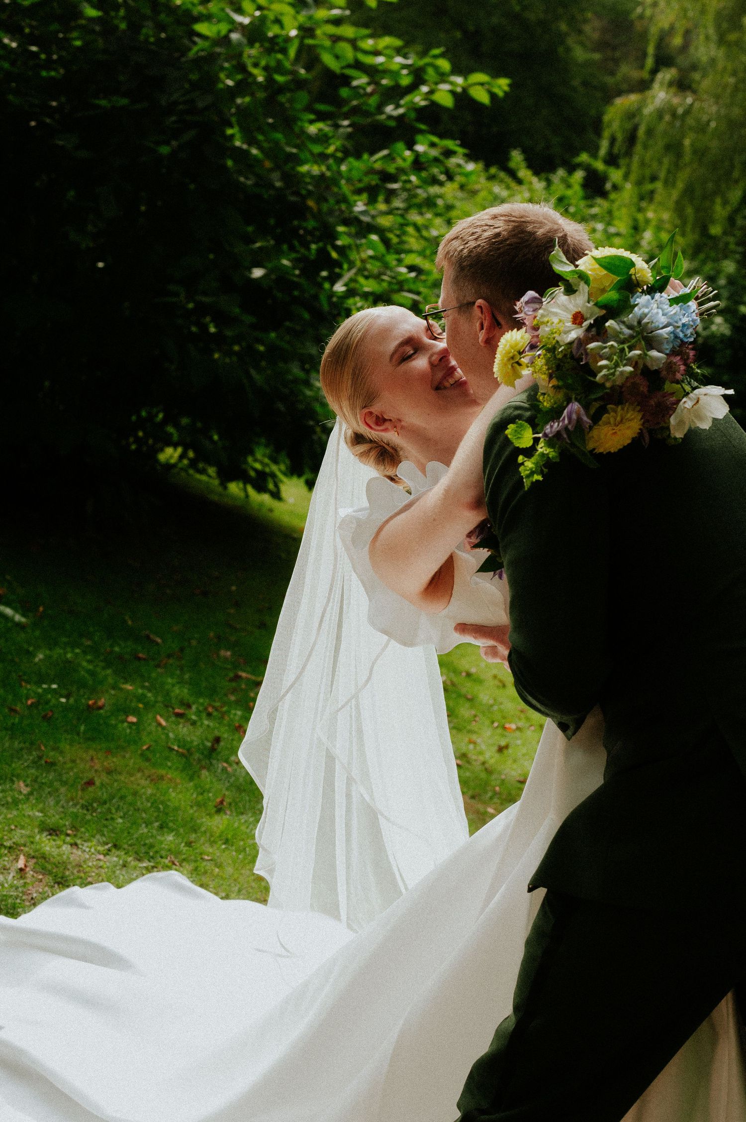 A romantic wedding moment captured in a lush garden setting with a flowing white dress and beautiful floral bouquet.