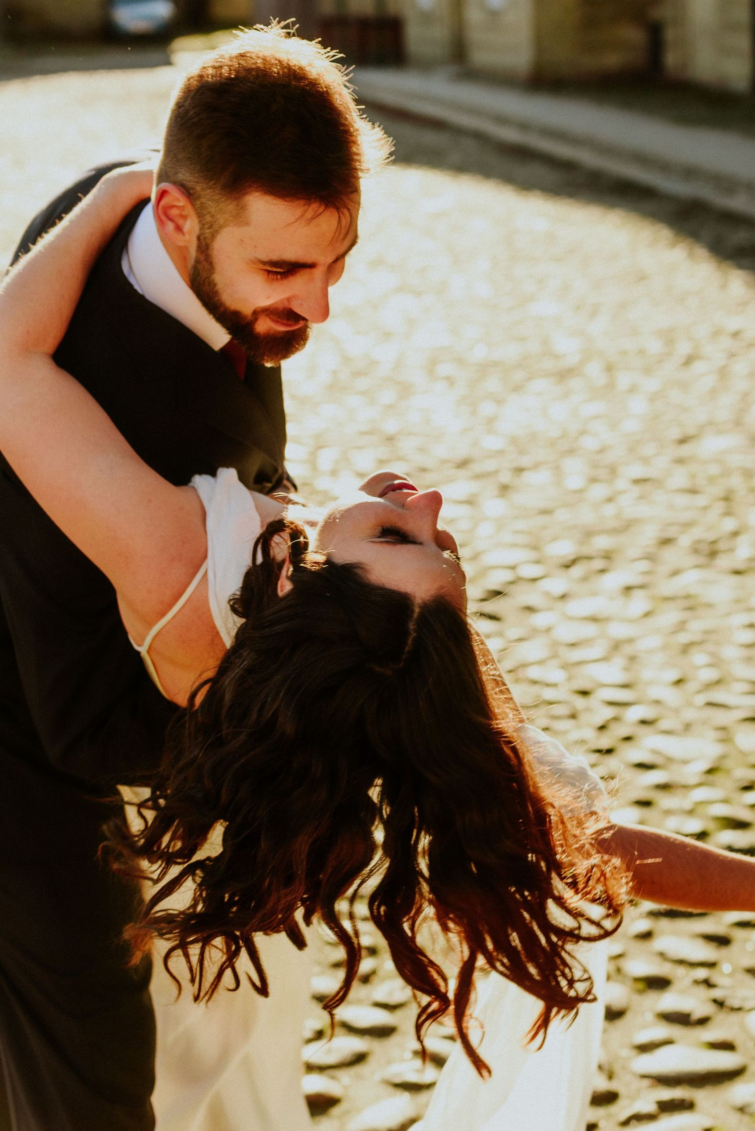 Artistic wedding photos capturing intimate moments between newlyweds at golden hour on cobblestone streets.
