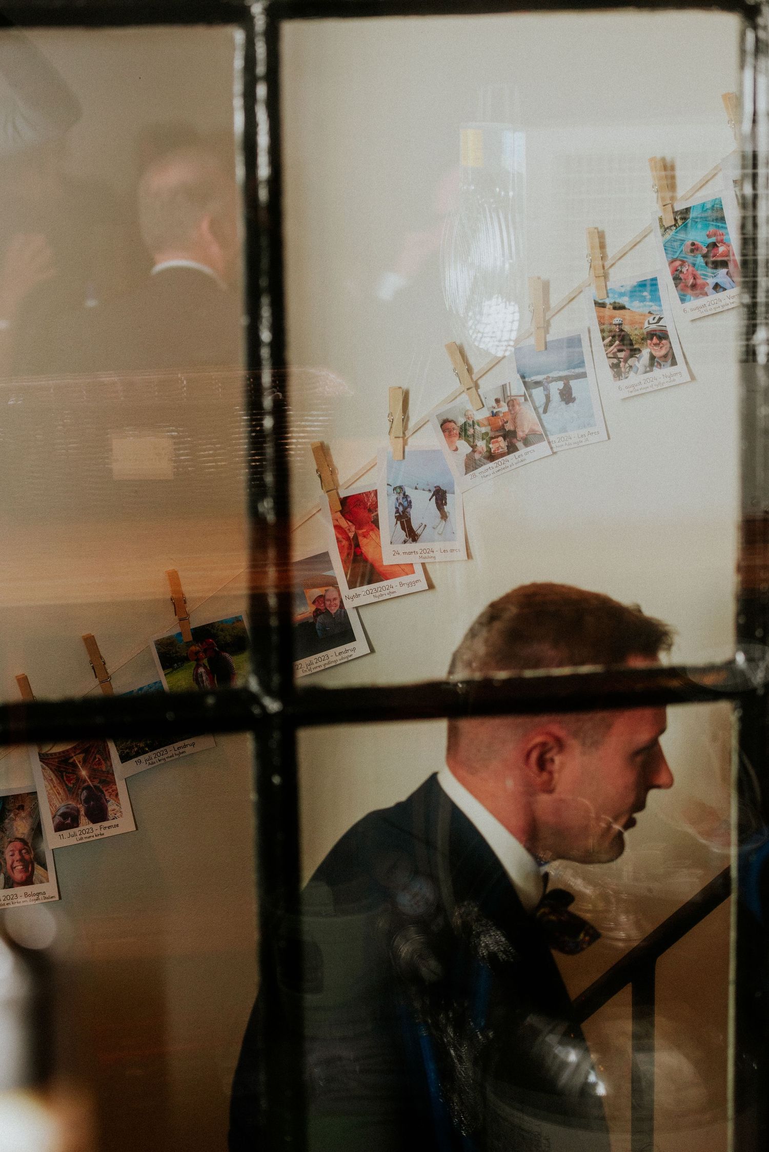 Person in dark suit examines photos displayed on wall with wooden clothespins in dimly lit room.