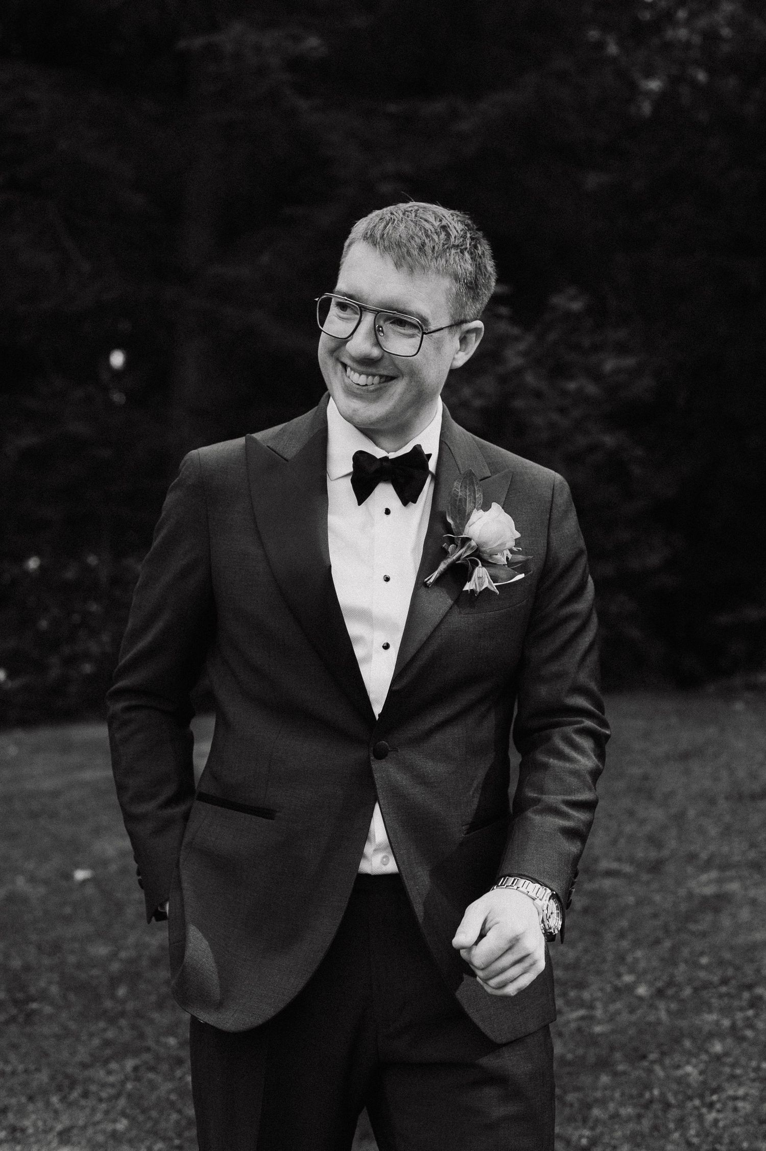 Groom in classic black tuxedo and bow tie smiles during outdoor wedding portraits.