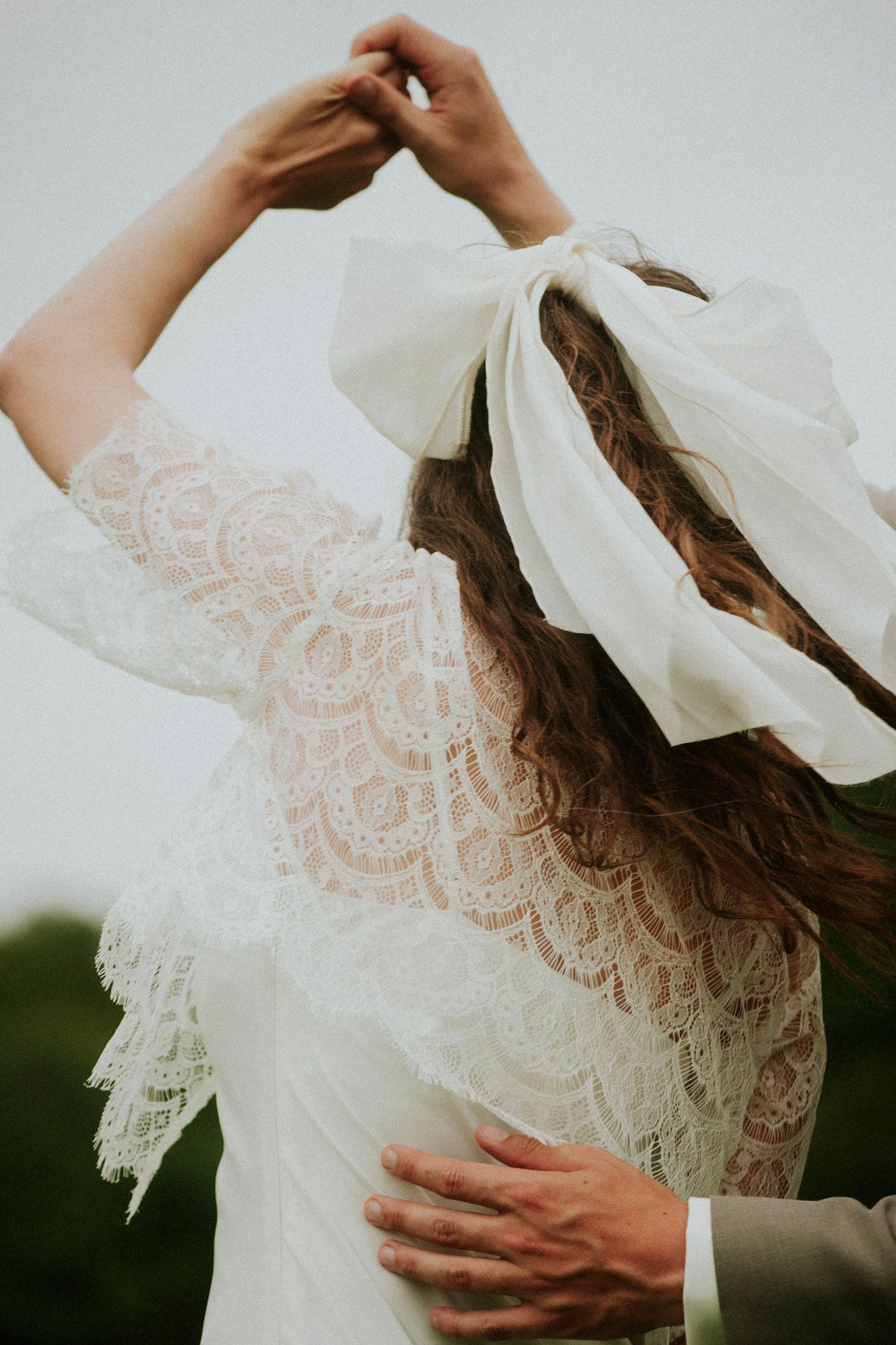 Detail shot of bride's lace dress and flowing veil being lifted by the wind.
