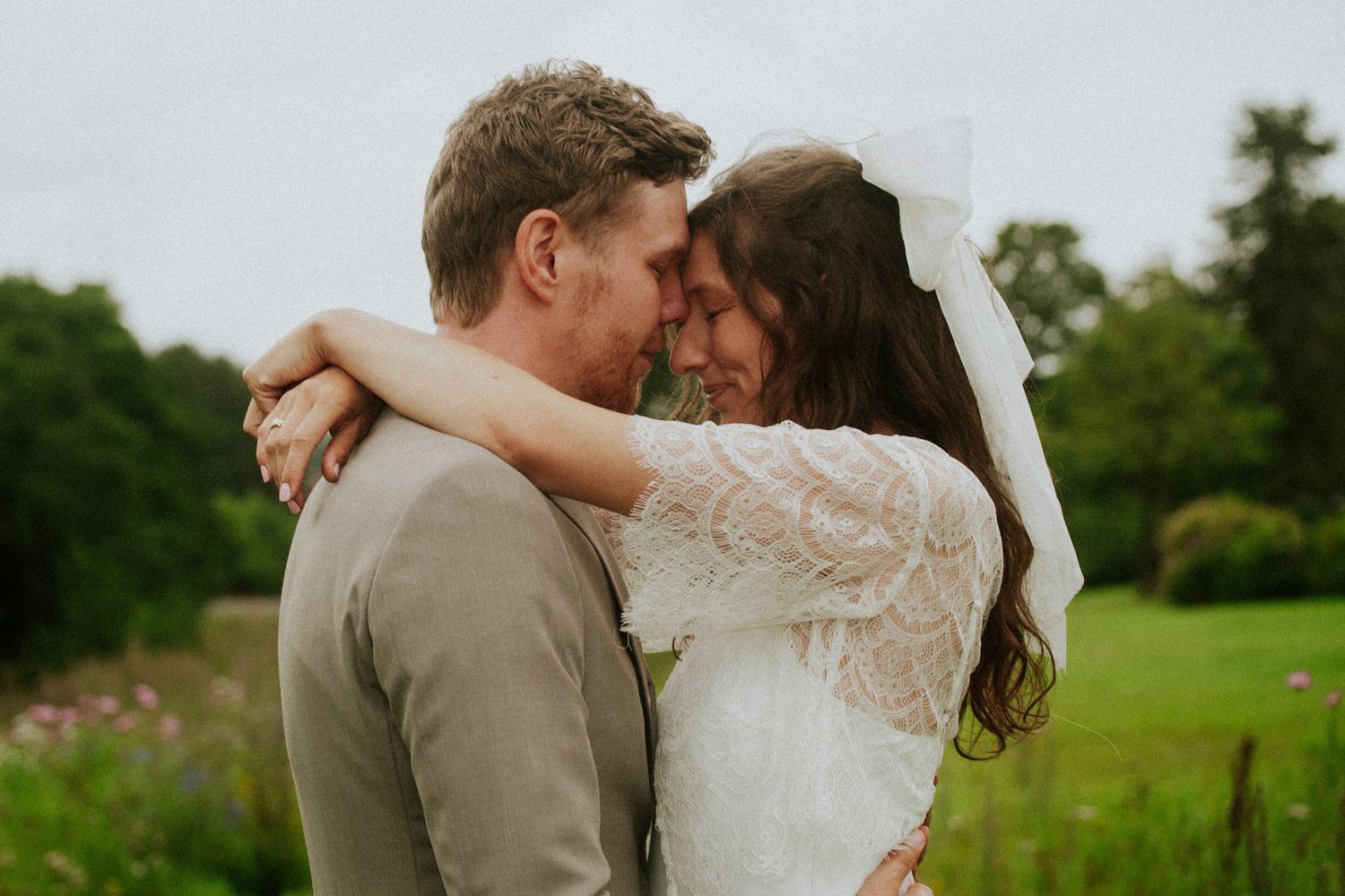 Romantic couple embraces and kisses in a lush green field during golden hour.