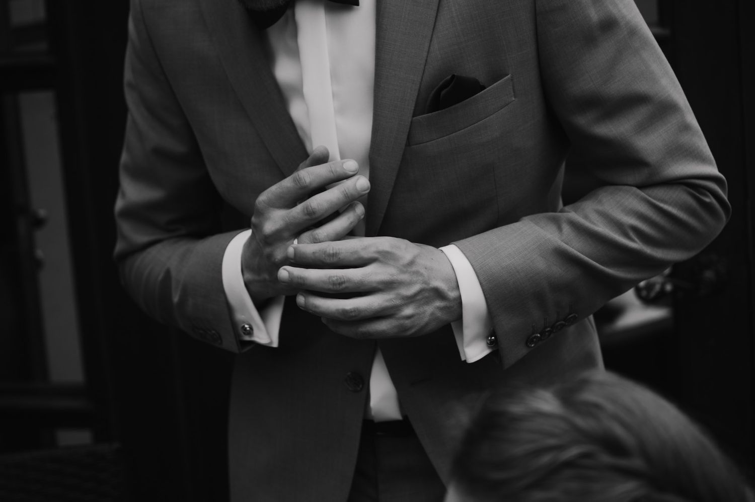 Close-up black and white shot of a groom adjusting his suit jacket and cufflinks.
