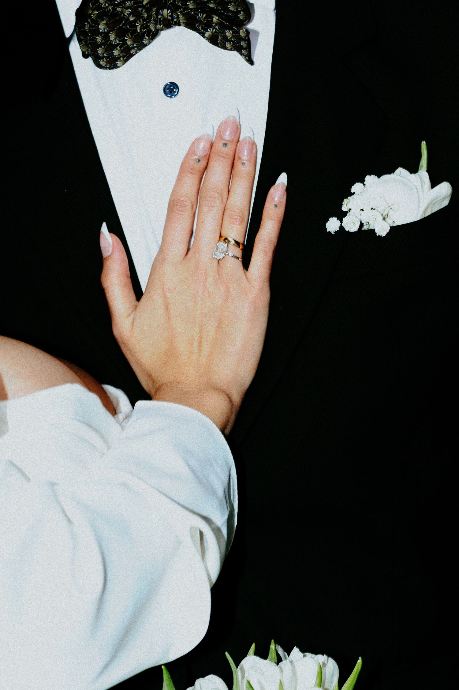 Manicured hand with engagement ring shown against a white and black background with floral accents.