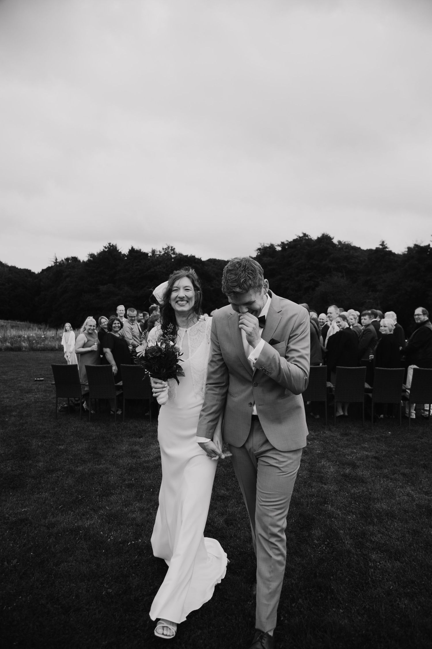 A candid black and white moment of laughter between newlyweds in an outdoor setting.