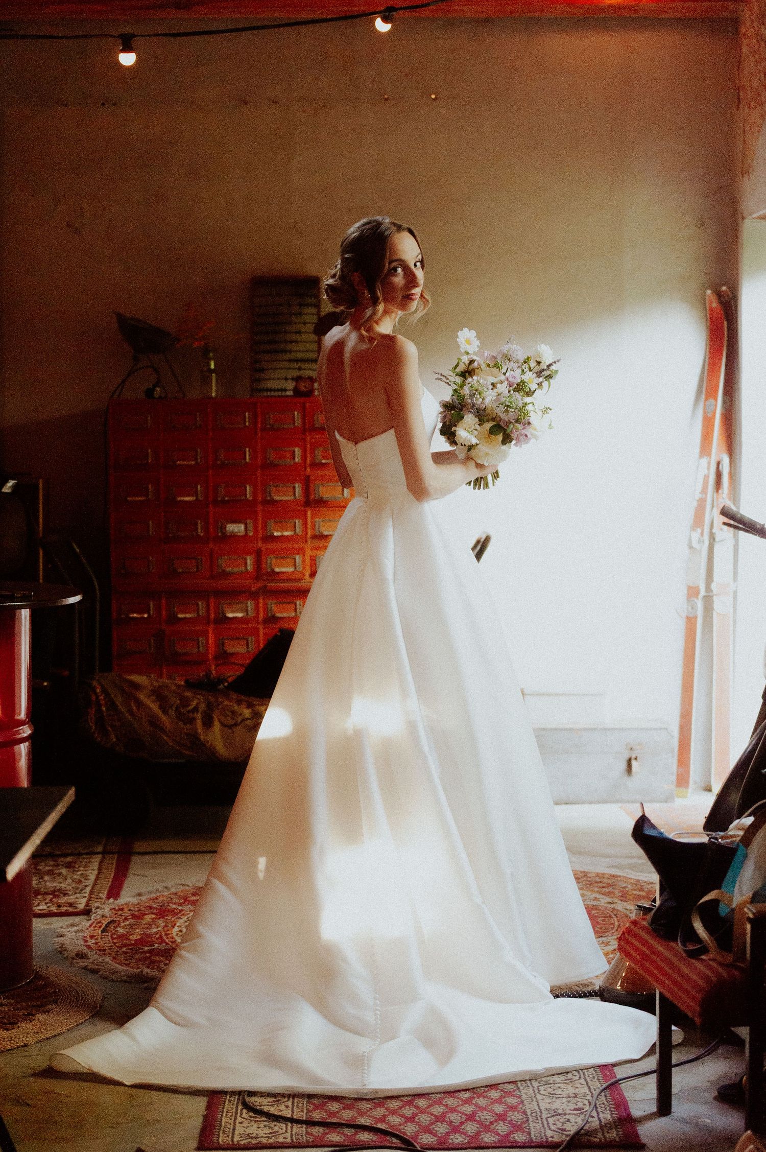 A wedding dress flows gracefully in a series of artistic photos taken against red lockers in a vintage-style setting.