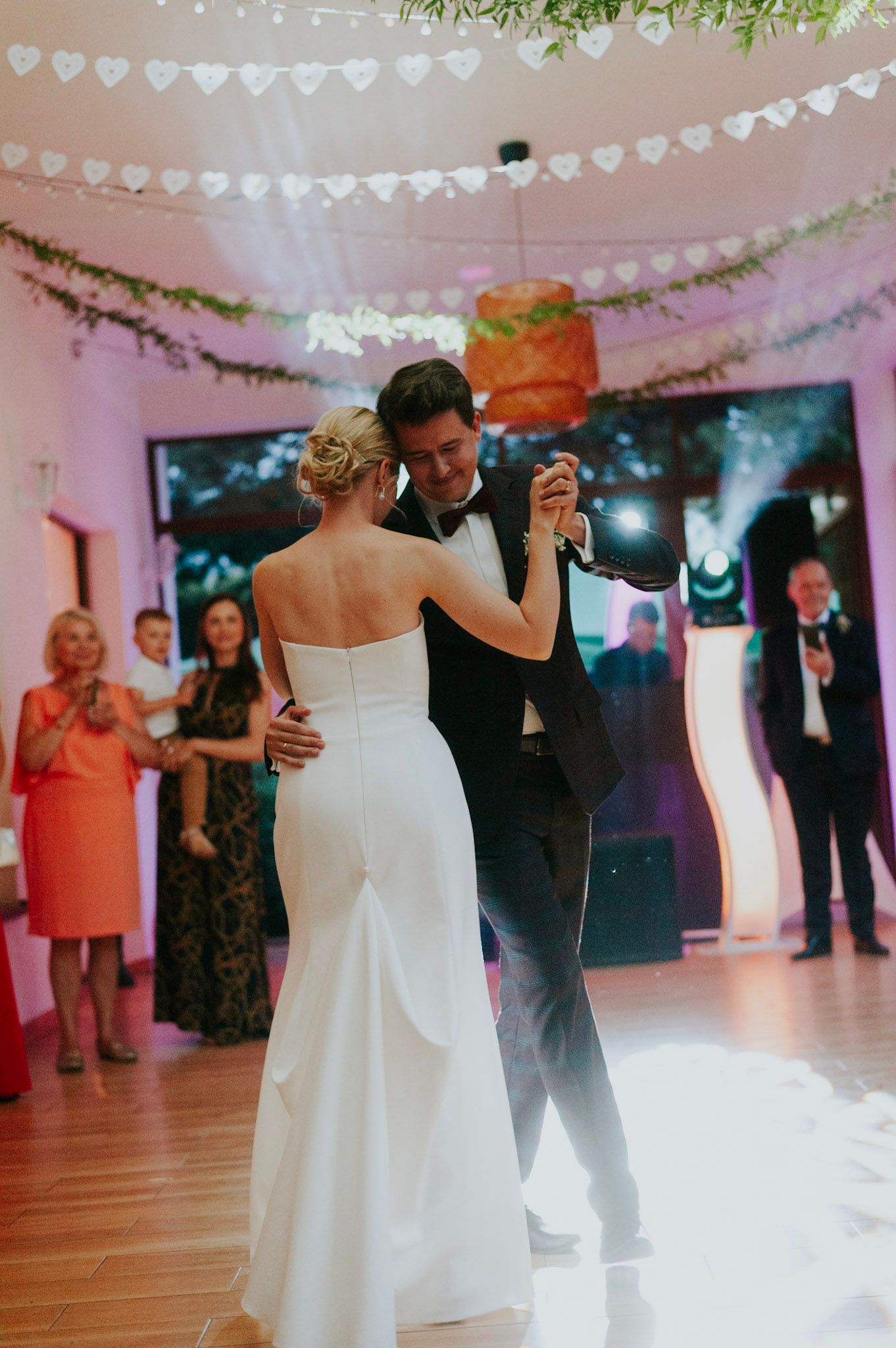 Newlyweds sharing their first dance under heart-shaped banners and warm lighting in a decorated reception venue.