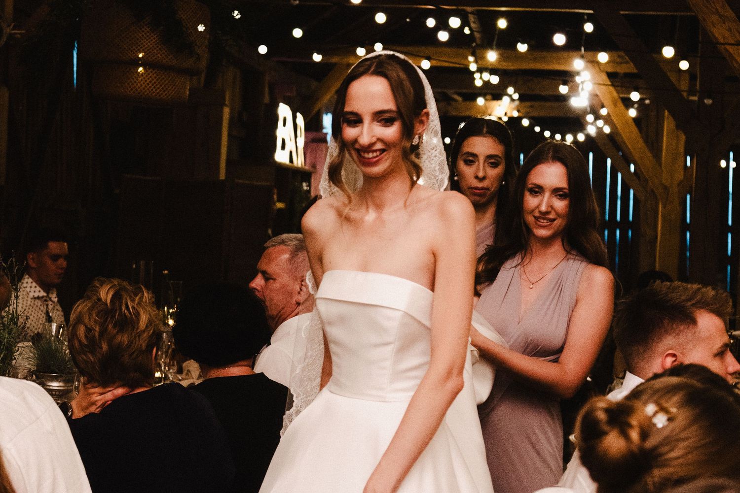 A couple dances together during a wedding reception with warm lighting and other guests in the background.