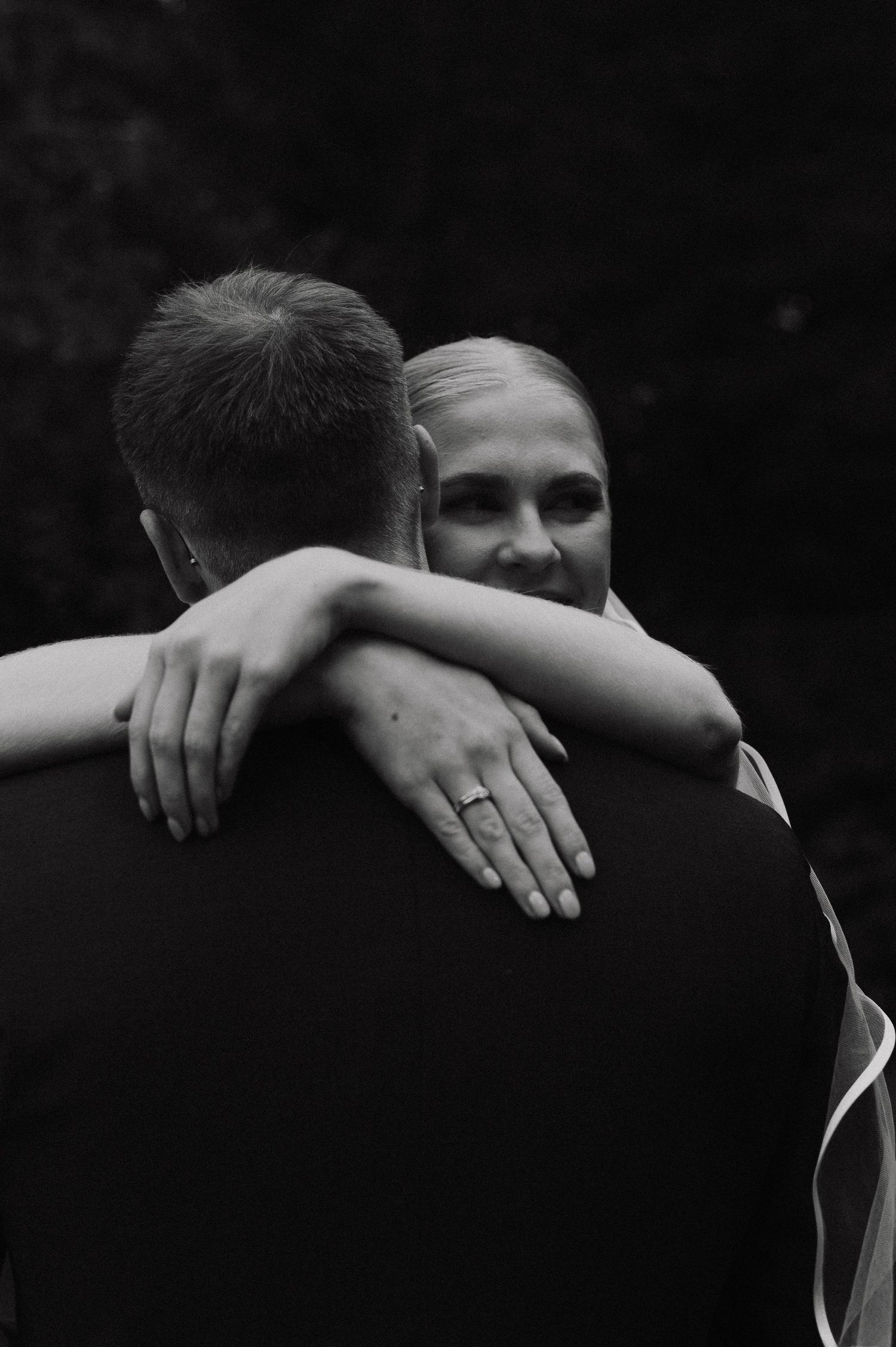 Black and white close-up of embracing couple showing hands and shoulders during an intimate moment.