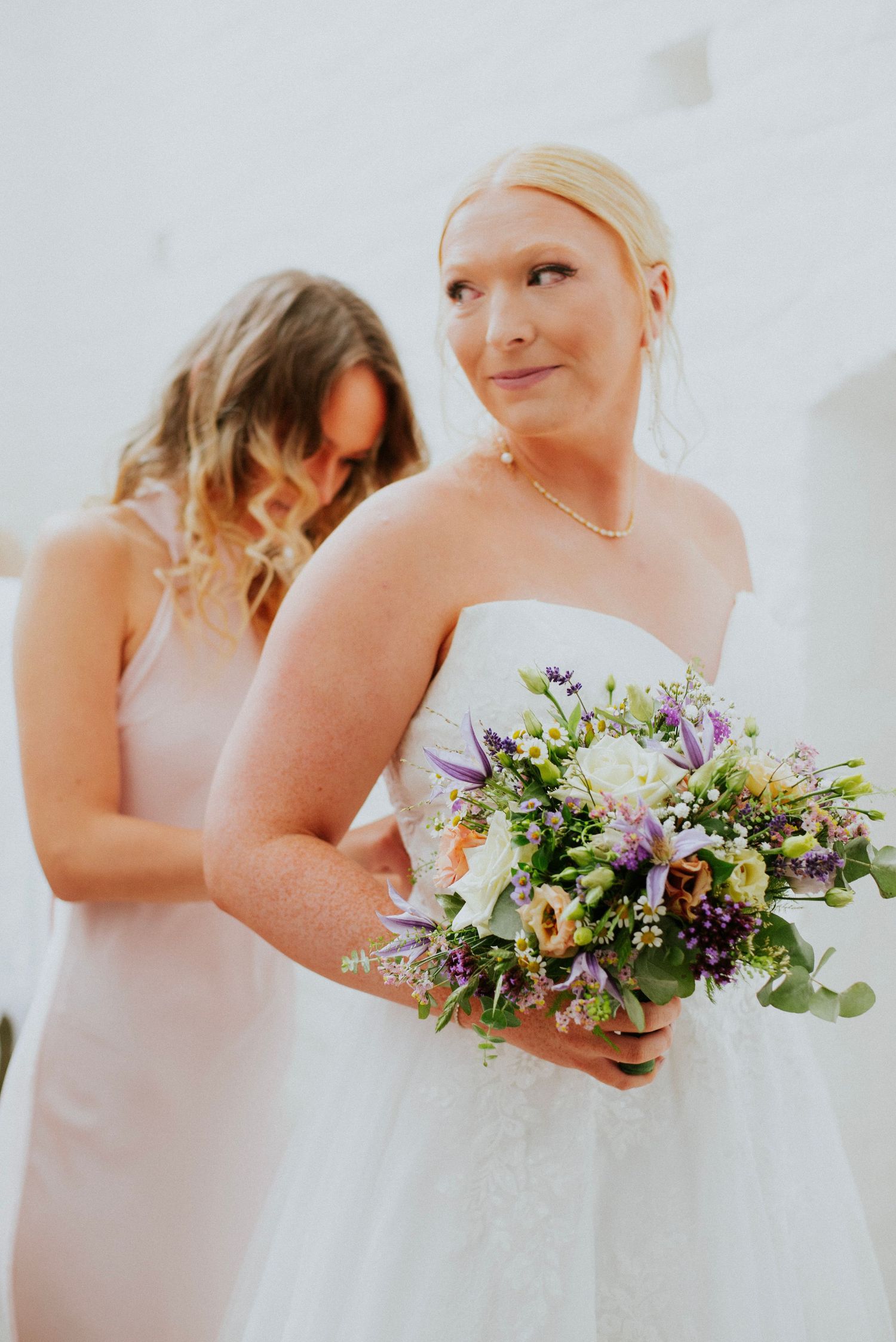 Bridesmaids in pink dresses holding colorful floral bouquets stand together.