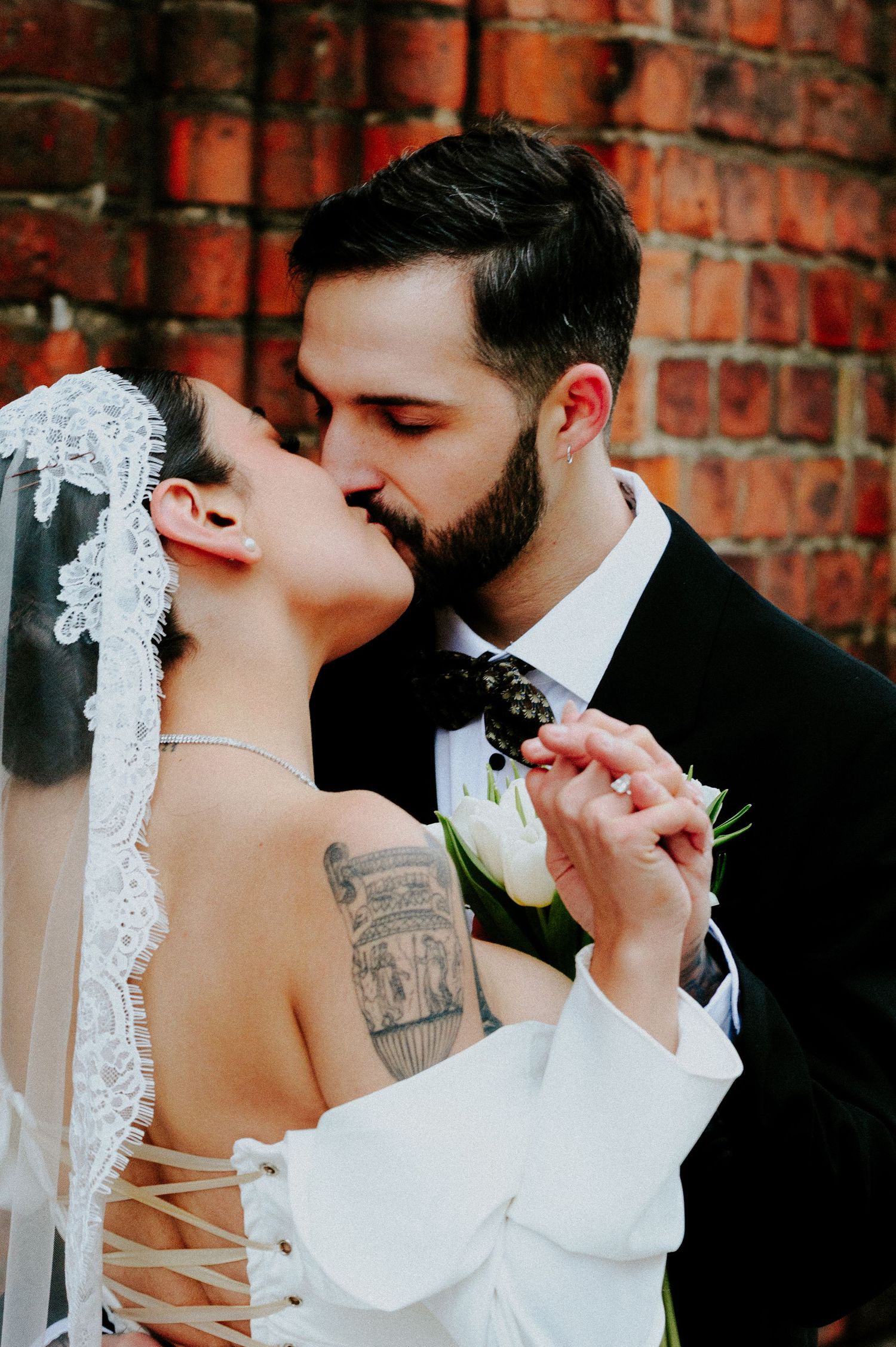 Romantic wedding portrait against brick wall showing tender embrace.