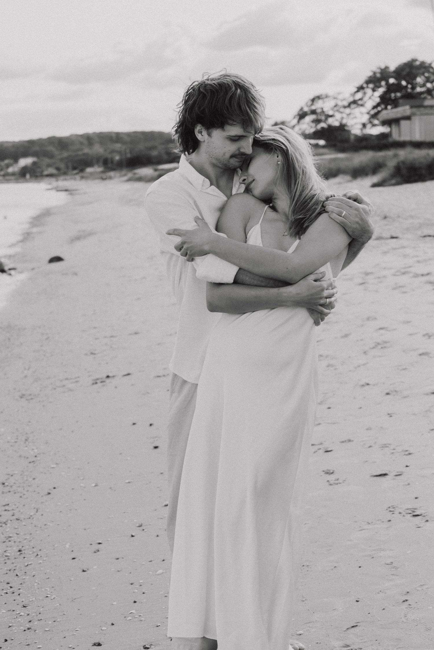 A romantic black and white photo series shows a couple embracing on a sandy beach.