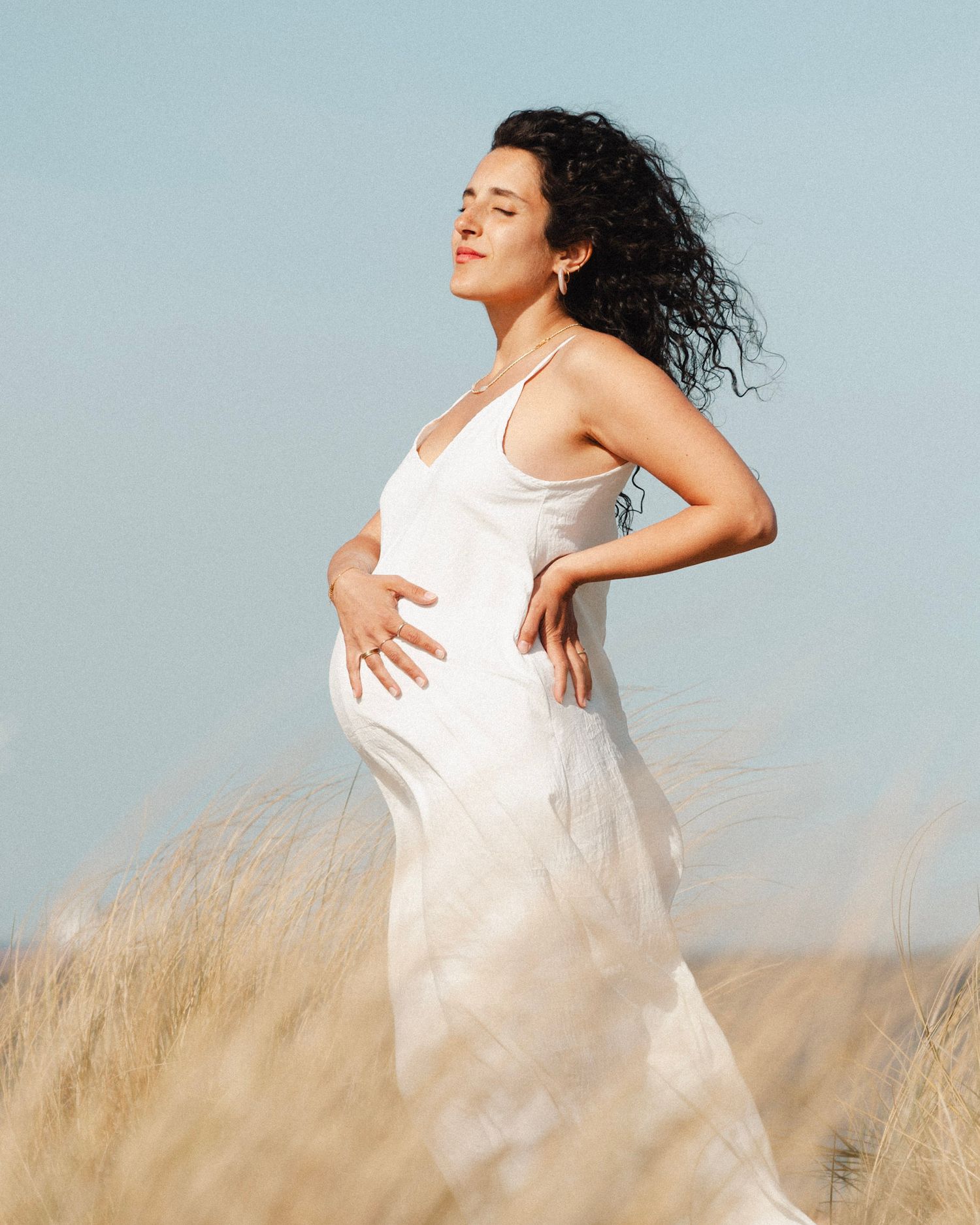 A woman in a flowing white dress dances gracefully through a field of golden wheat against a light blue sky.