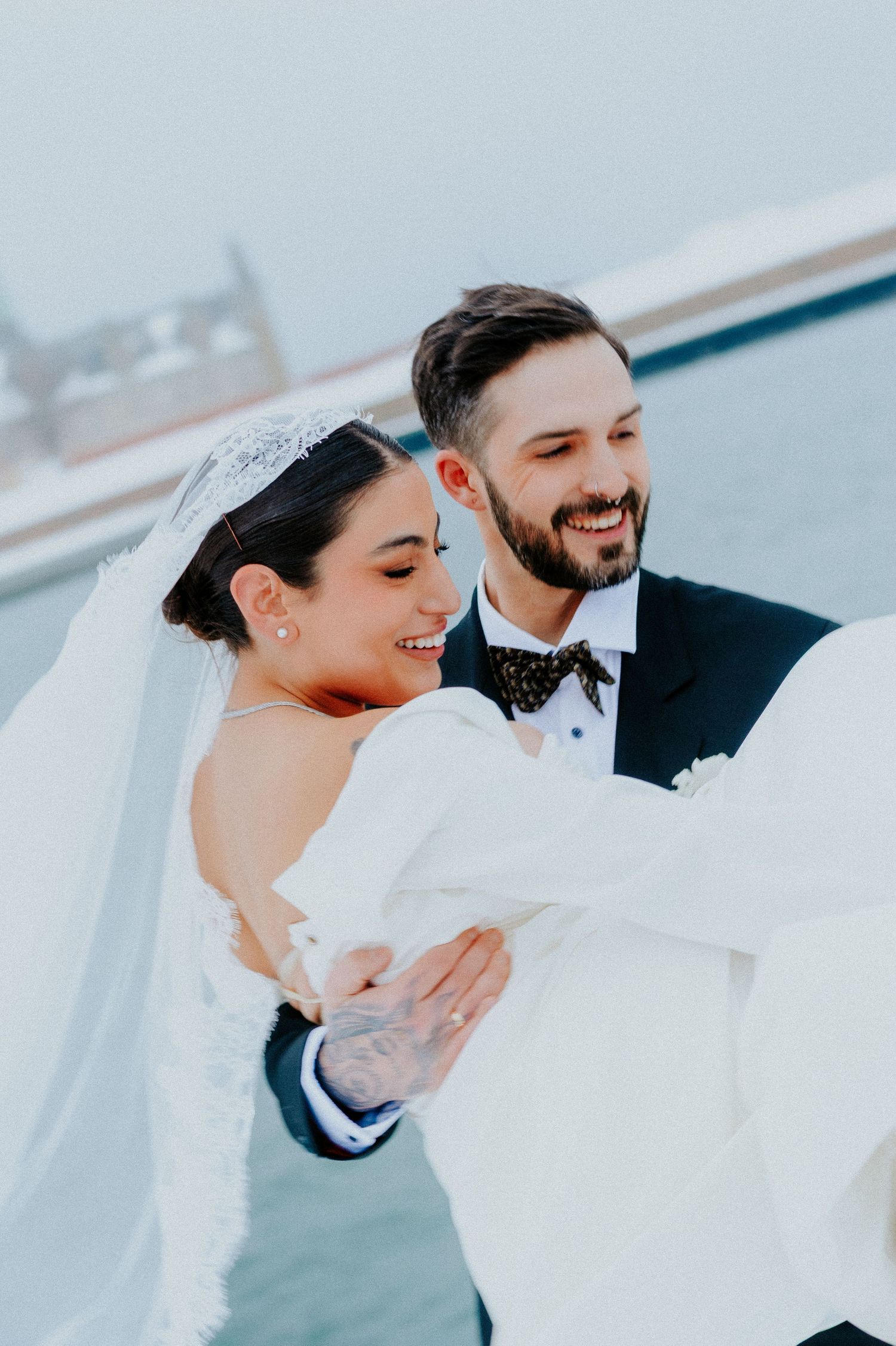 Joyful winter wedding portrait with couple laughing against snowy backdrop.