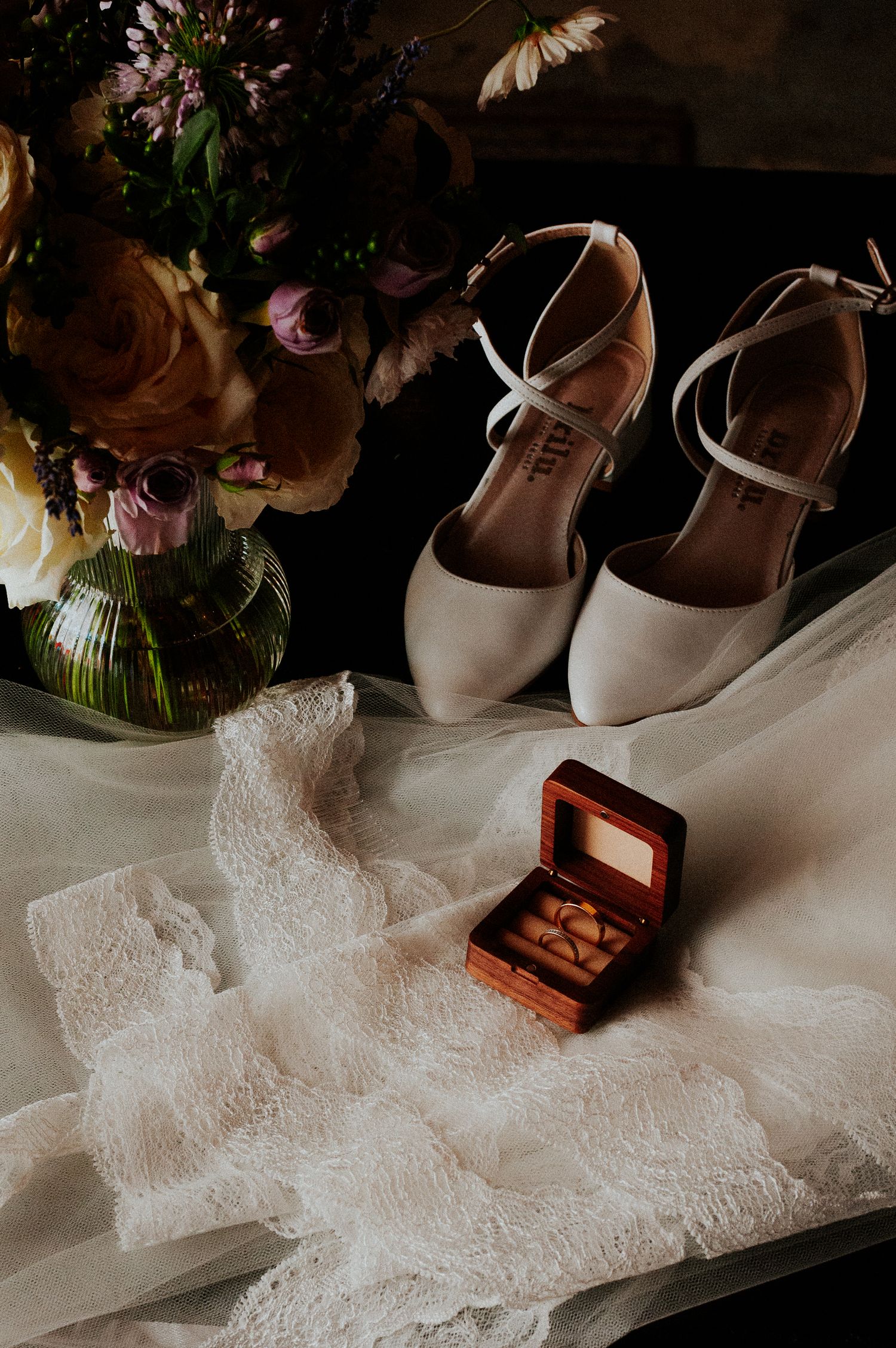 Wedding details featuring elegant beige shoes, delicate lace fabric, and a small wooden ring box in a romantic arrangement.