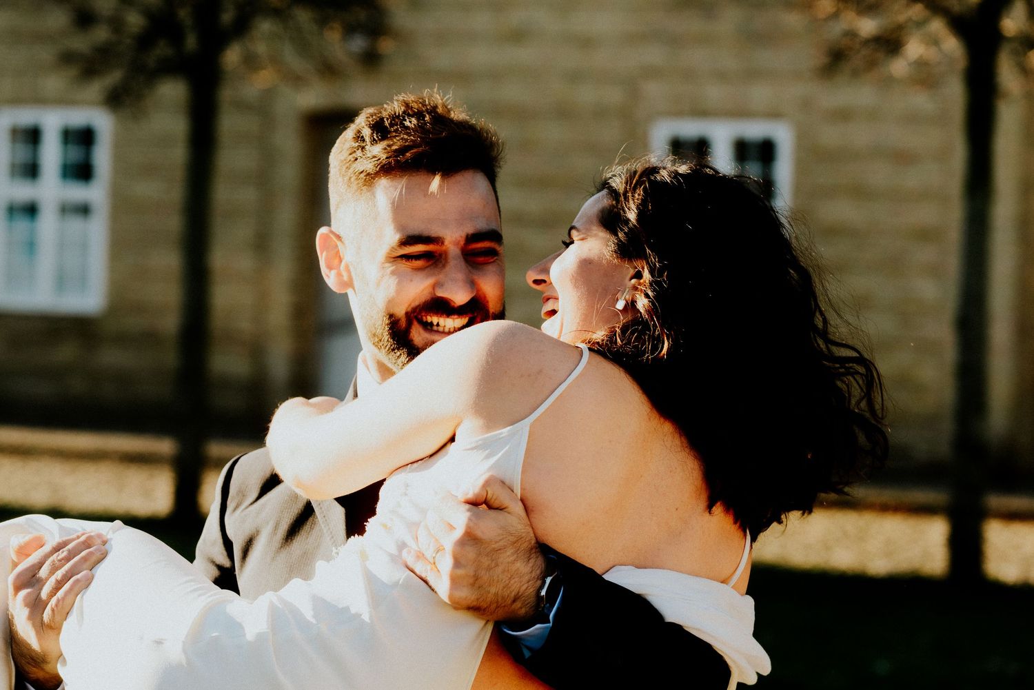 Groomsmen celebrate with laughter and hugs during an outdoor wedding celebration on a sunny day.