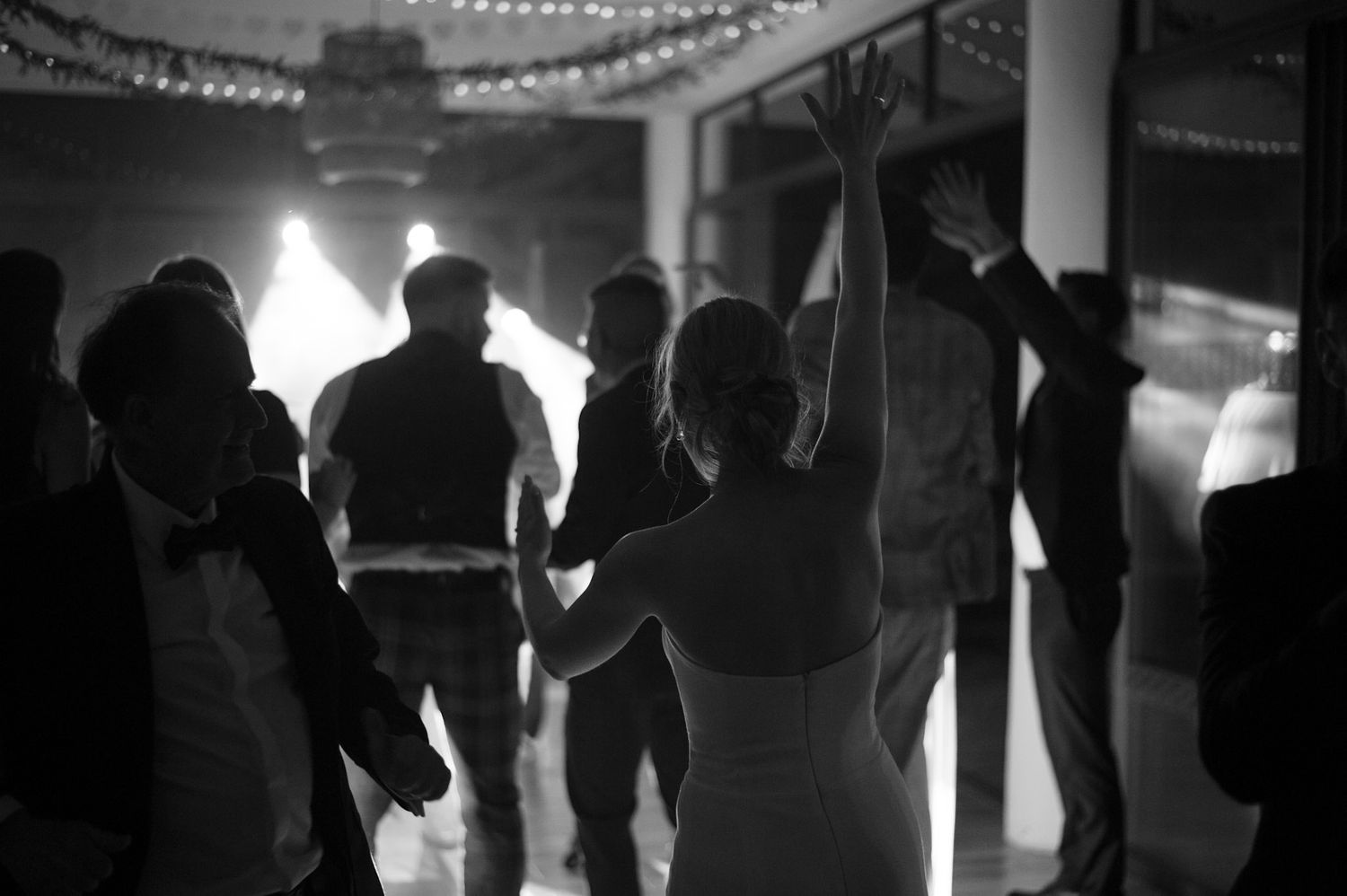Silhouetted wedding guests dancing and celebrating in dimly lit reception space.