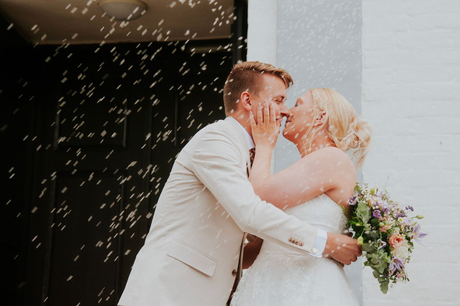 Intimate wedding moment captured in a bright interior setting with confetti falling.