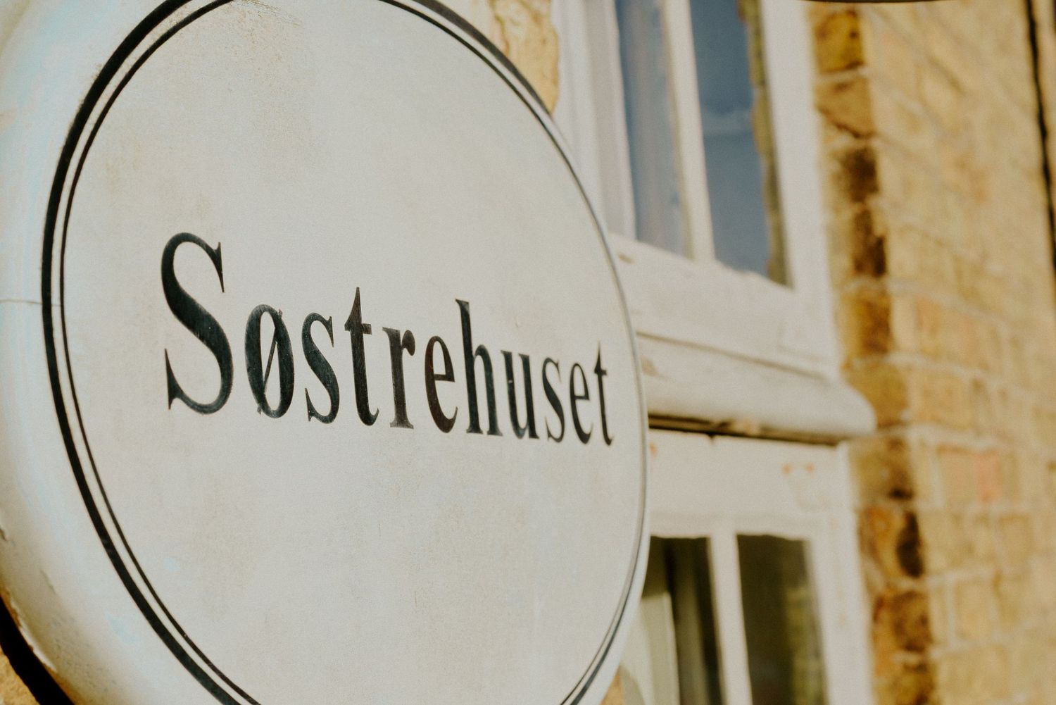 Vintage-style storefront signs with 'Sostrehuset' text mounted on a light colored building exterior.