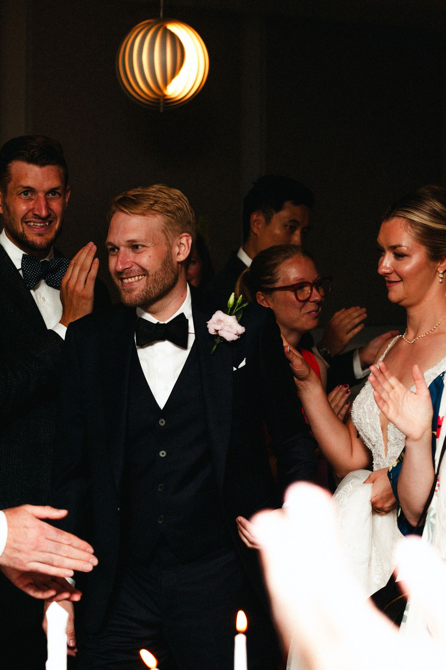 Wedding celebration at night with guests in formal attire gathered under a modern pendant light fixture.