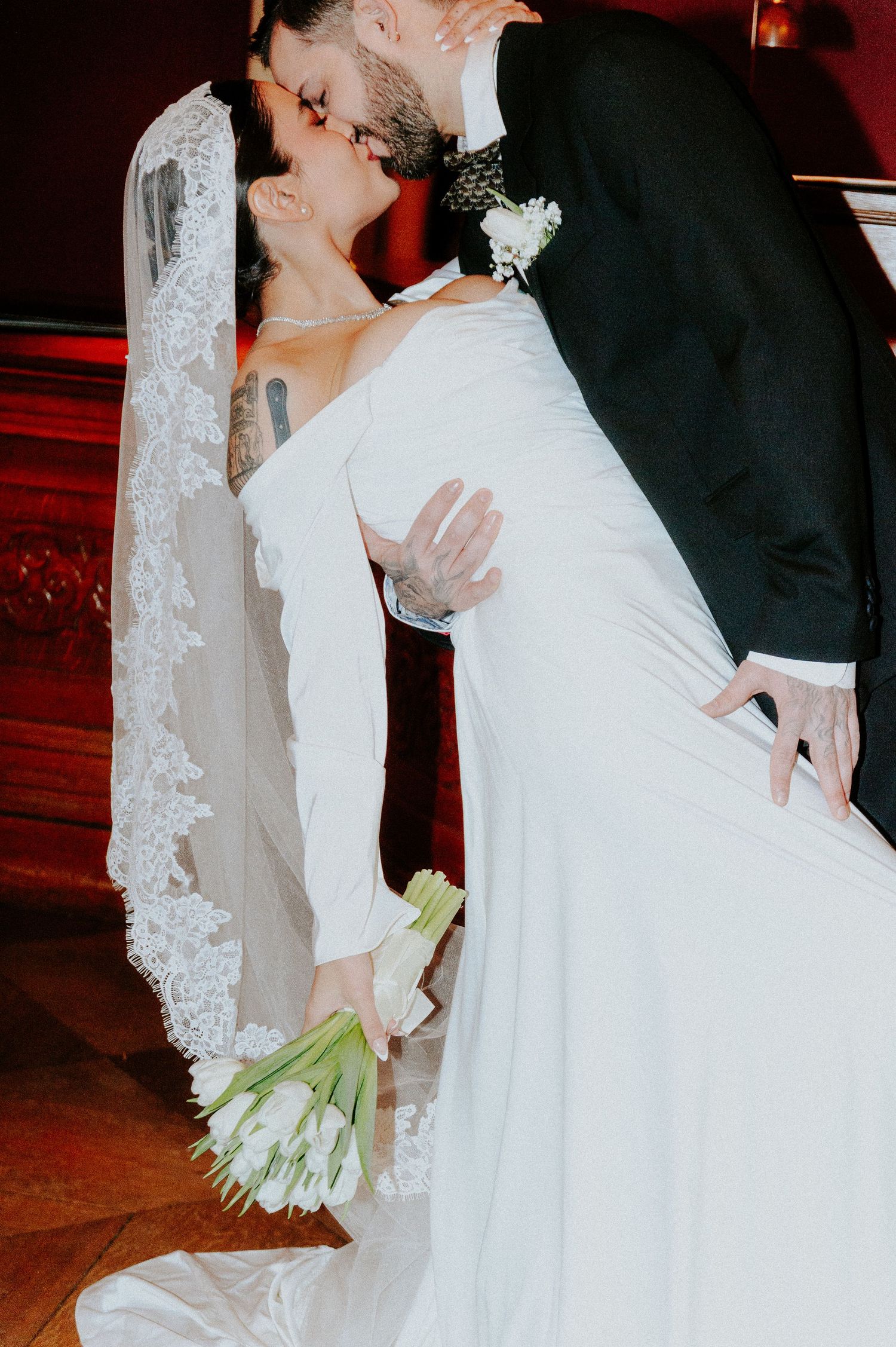 Elegant bride in lace veil holds white tulip bouquet during wedding ceremony.