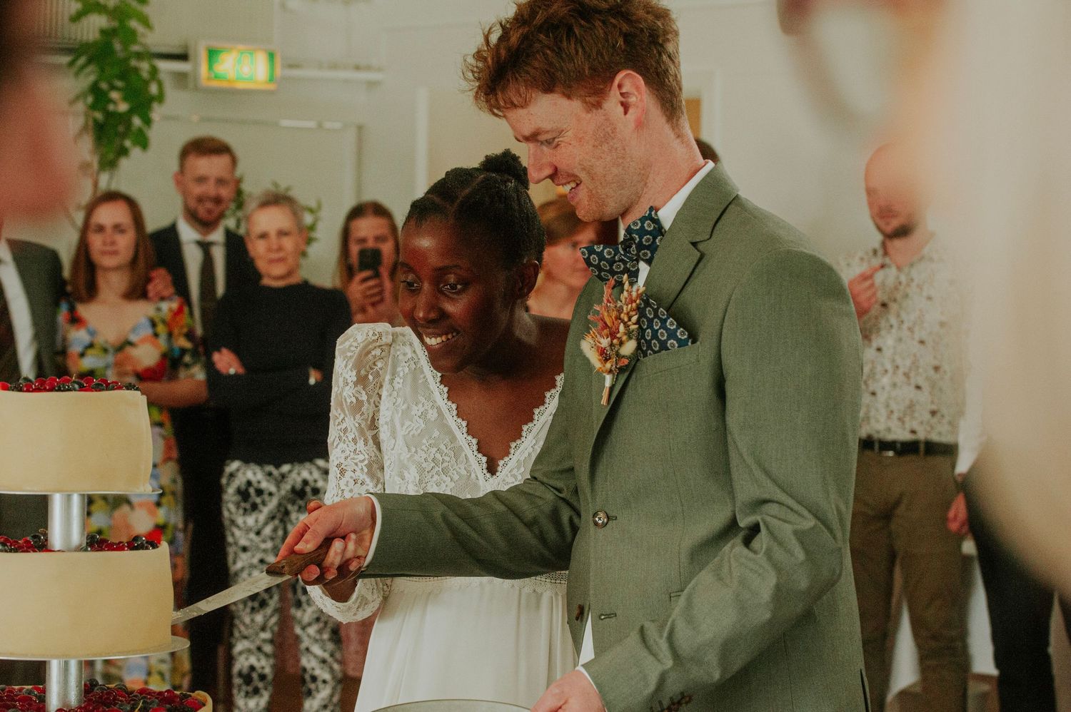 Wedding couple cutting their cake together while surrounded by guests at their reception.