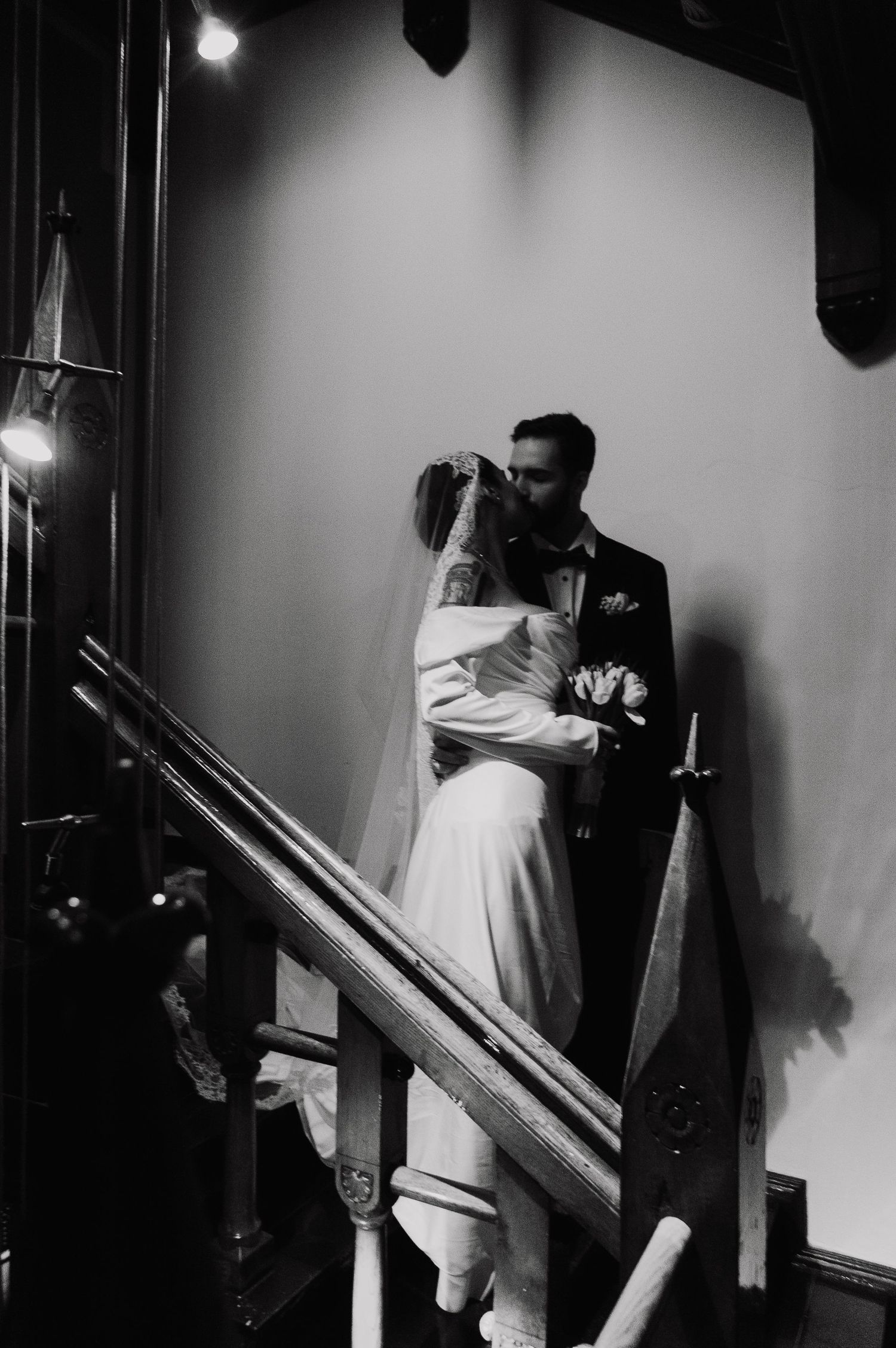 Artistic black and white photo of newlyweds embracing on vintage staircase.