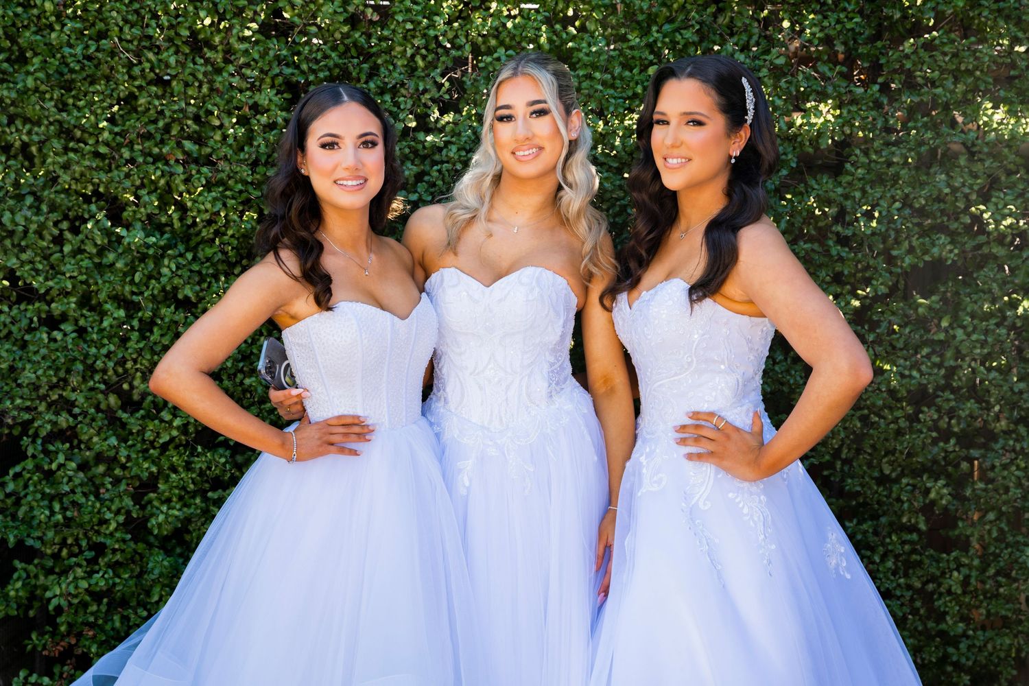 Women wearing white bridesmaid dresses pose together at an outdoor garden wedding celebration.