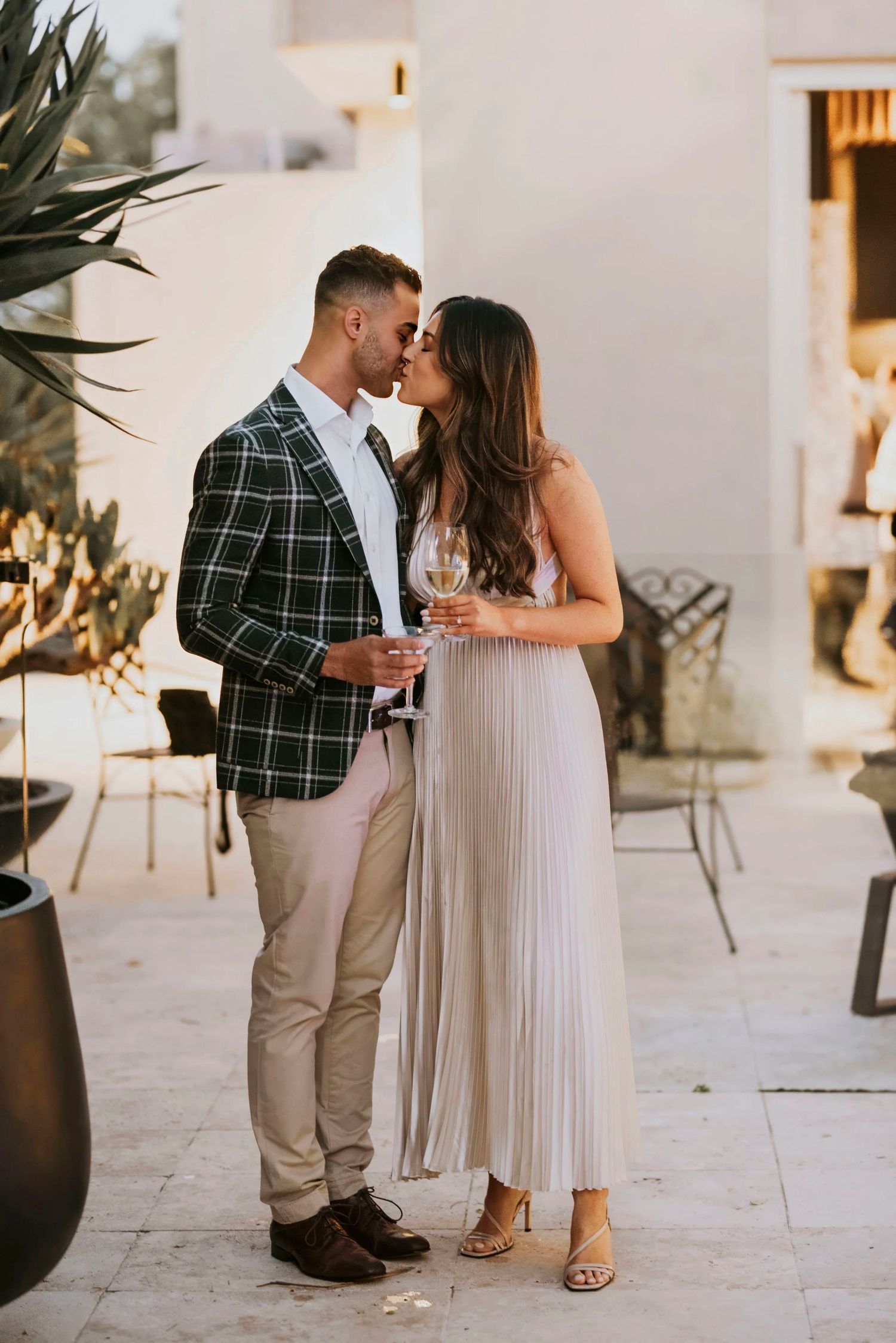 Romantic couple in elegant attire sharing an intimate moment on an outdoor patio at sunset.