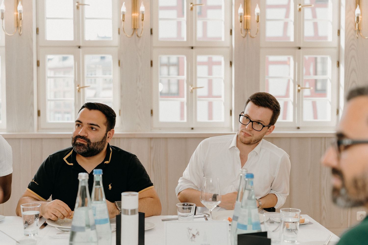 Two men sitting at a conference table in a bright room, engaged in a business meeting discussion.