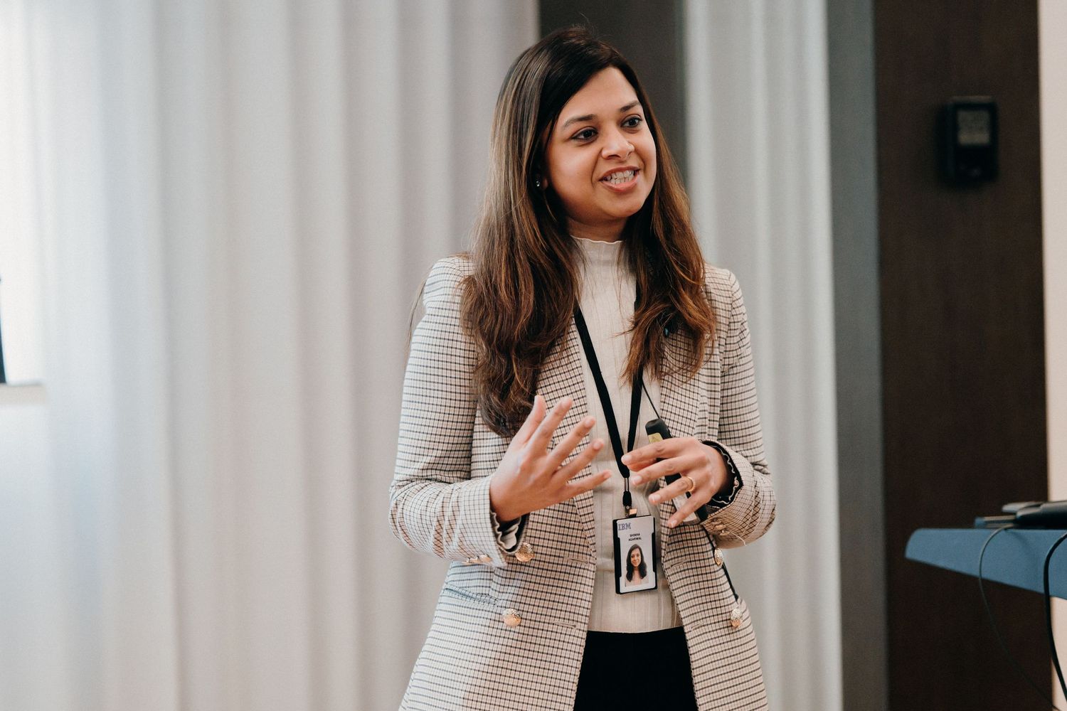 Professional woman in beige blazer and black top smiles while presenting in modern office setting.