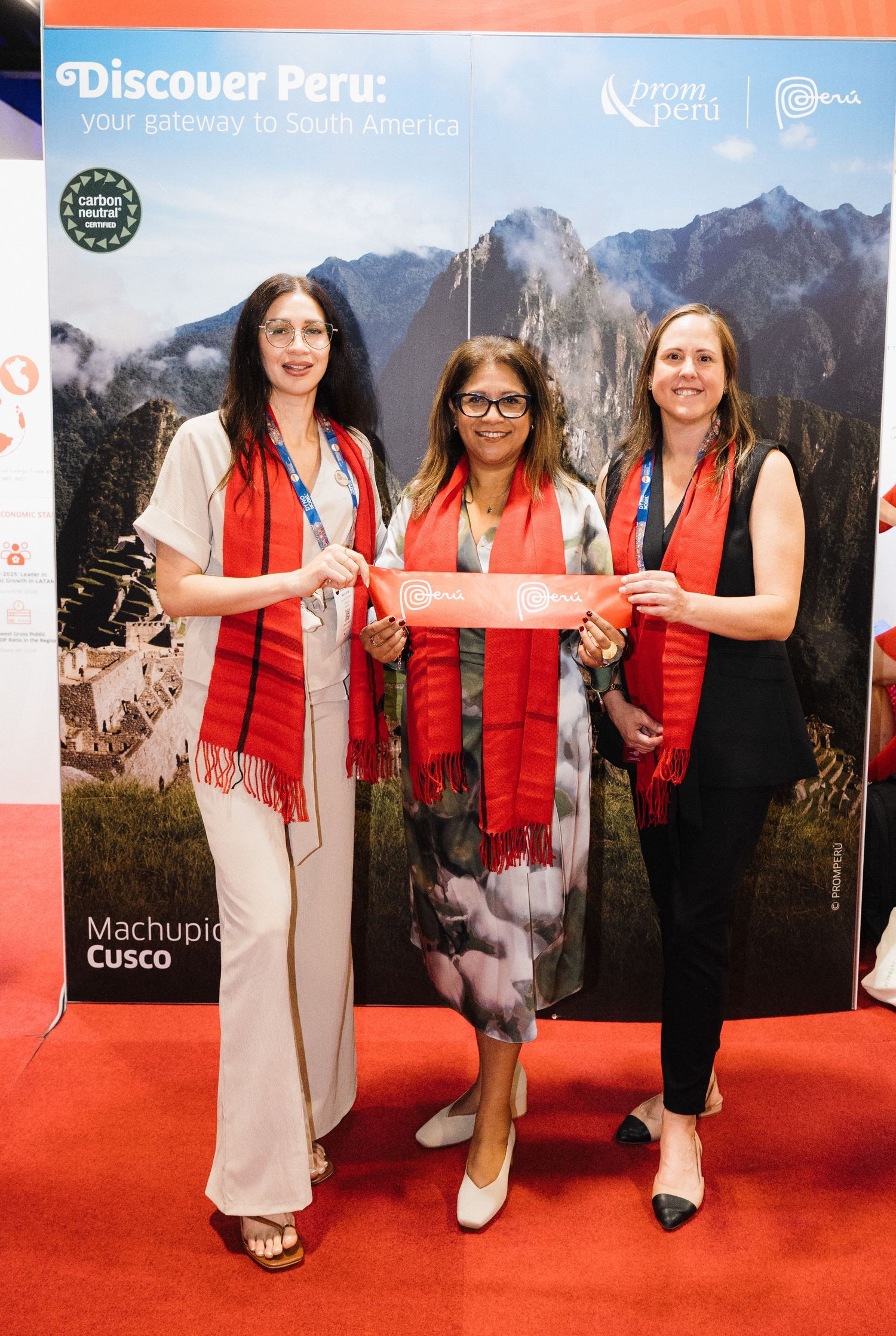 Group of friends in red scarves pose together at a tourism event with mountain backdrop display.