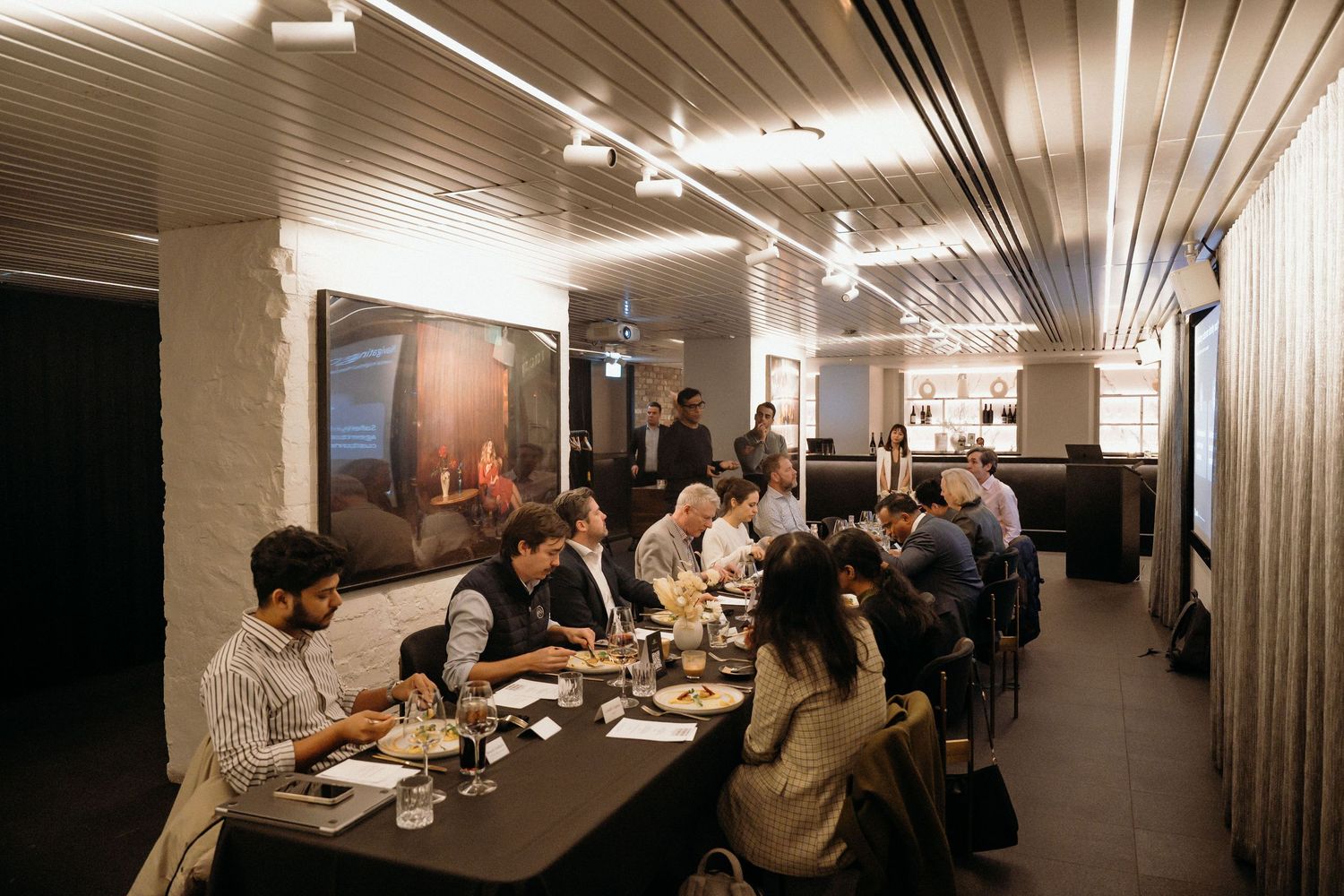 A panoramic view of people dining in a modern restaurant with wood-paneled walls and track lighting.