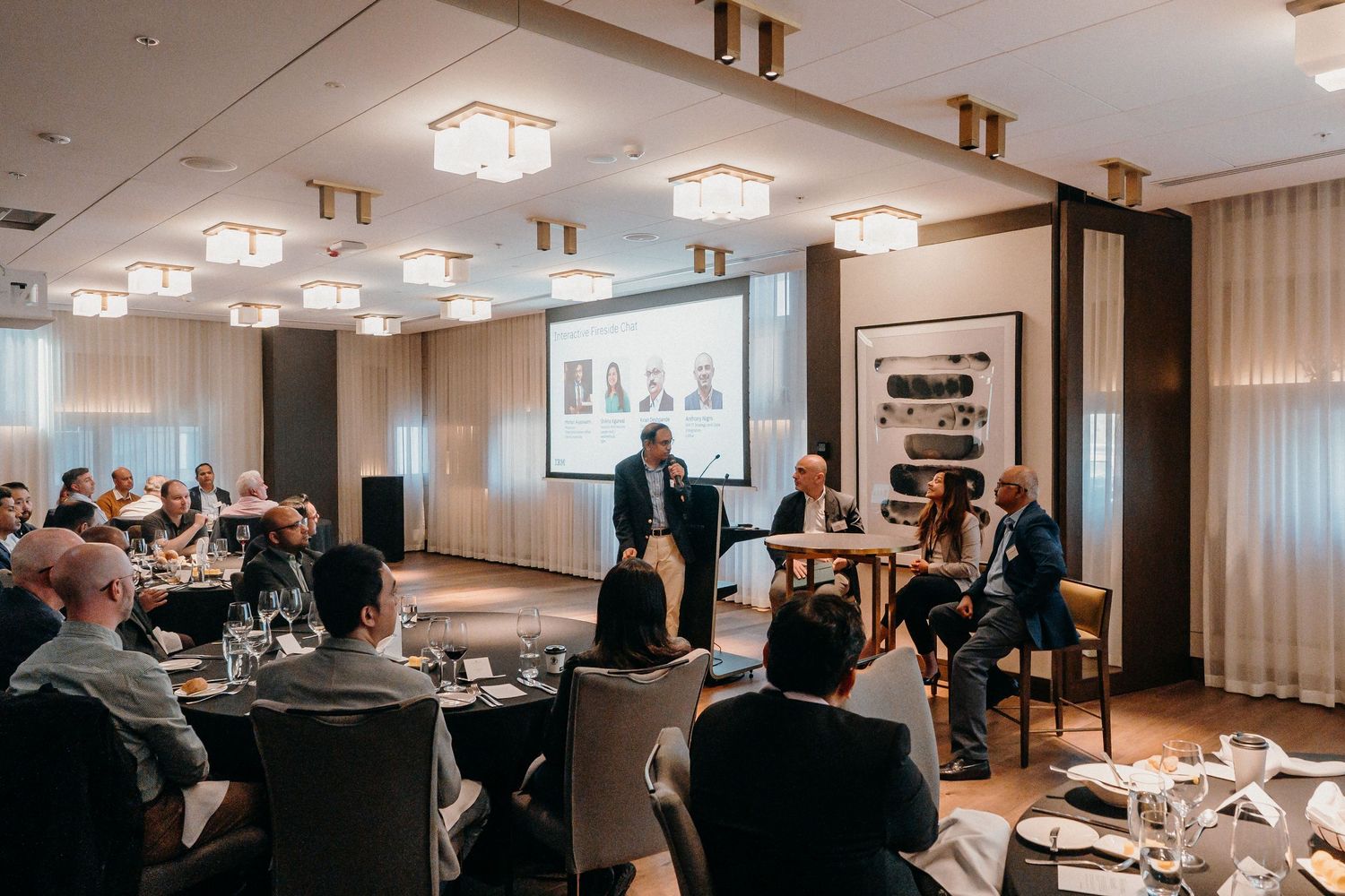 Business professionals gather in a modern conference room with white lighting fixtures and presentation screens.