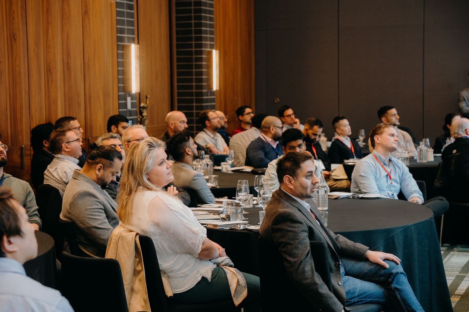 Business professionals sitting at tables during a corporate conference or training event in a modern meeting room.