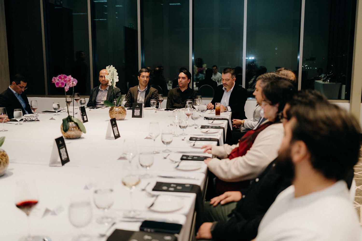 Business professionals seated at a long table during a corporate dining event with wine glasses and place settings.