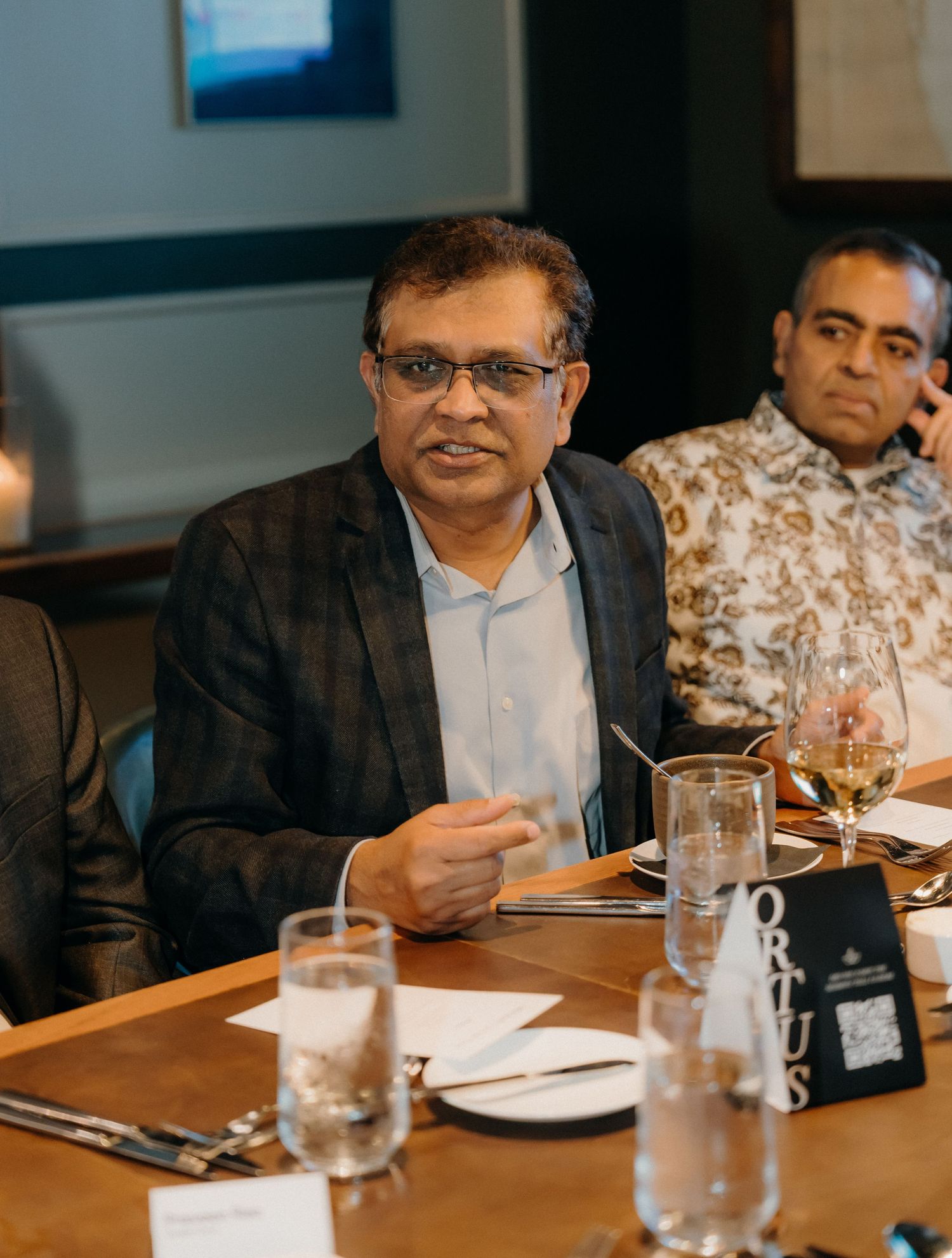 Business professionals seated at a conference table during a meeting with water glasses and papers visible.