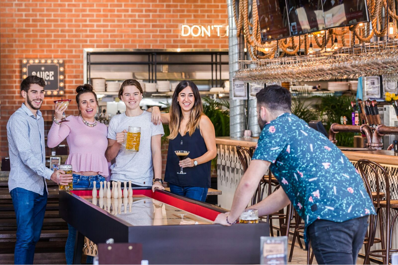 A group plays foosball at a bar with brick walls and wooden decor in the background.