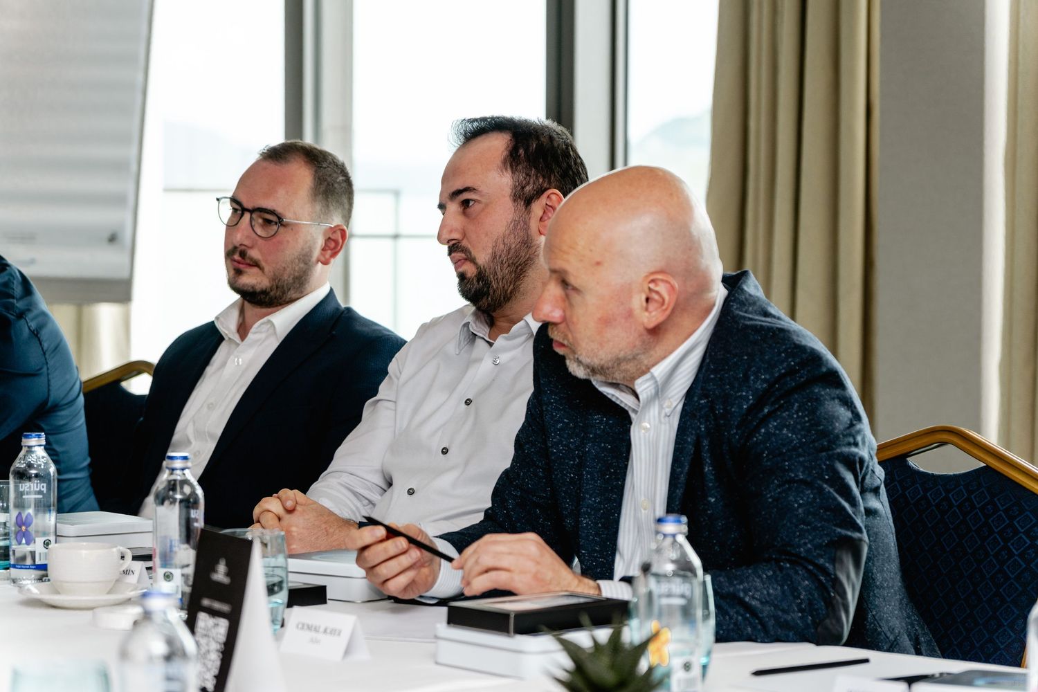 Three businessmen sitting at a conference table during a professional meeting in a modern hotel room.