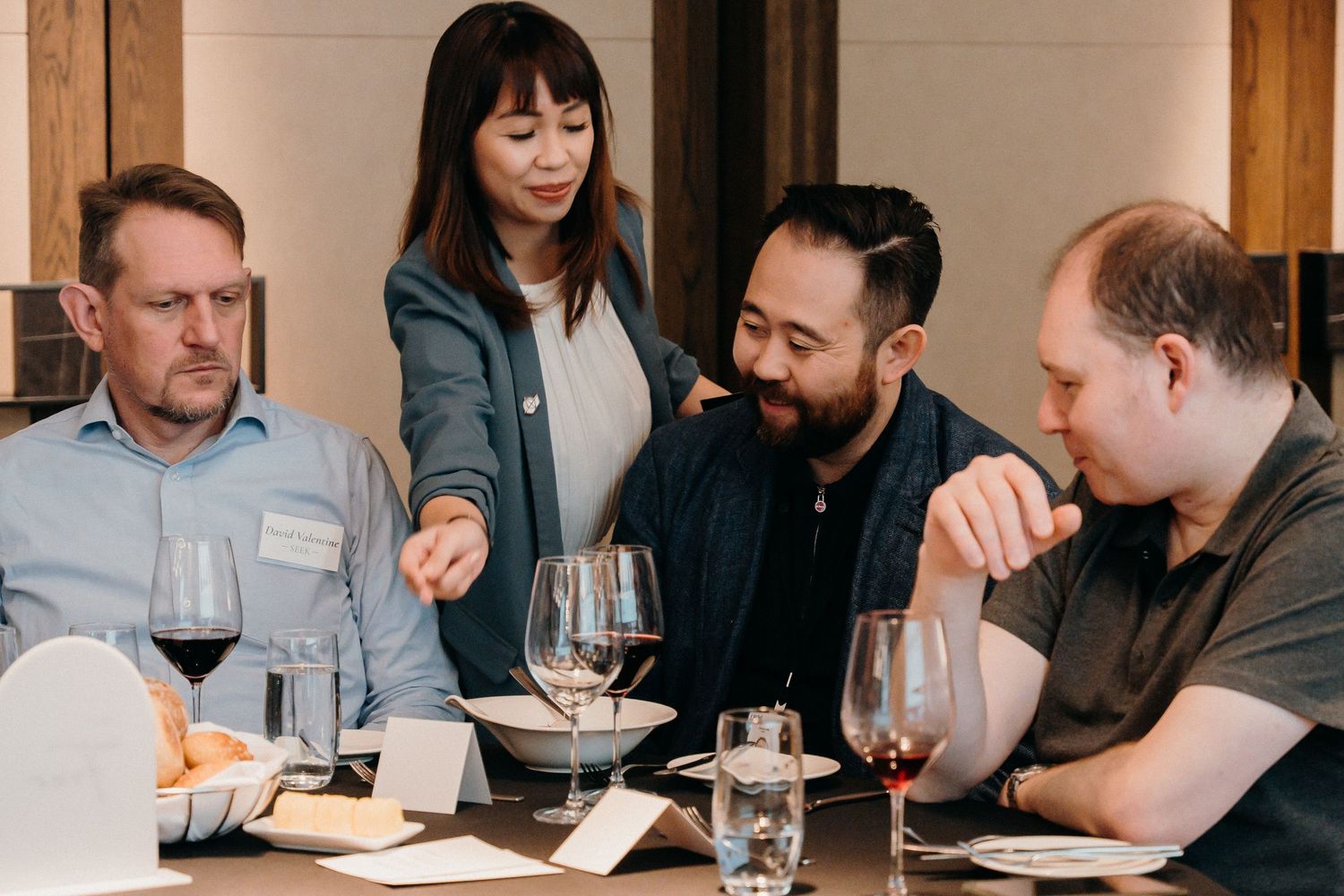 Business professionals gather around tables for a wine tasting event with notepads and glasses.