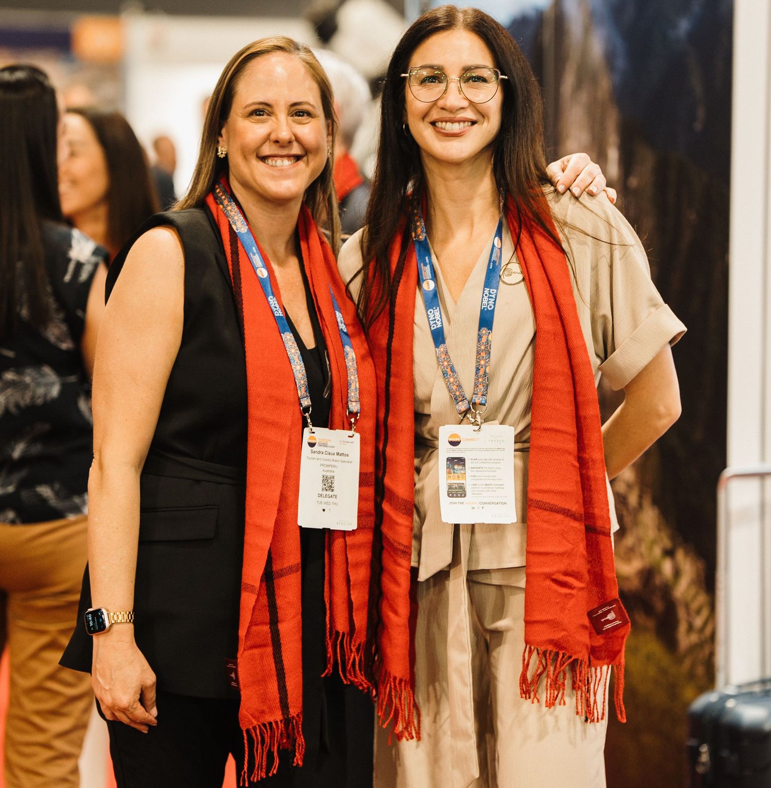 Colleagues in red scarves gather and smile during a professional networking event.