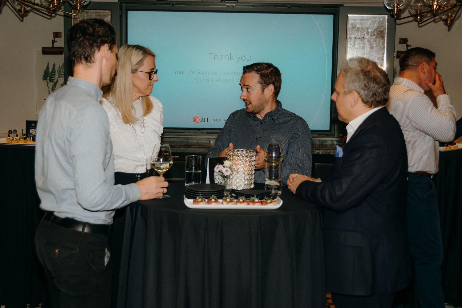 People gather around a table at a dimly lit social event with a dark tablecloth.
