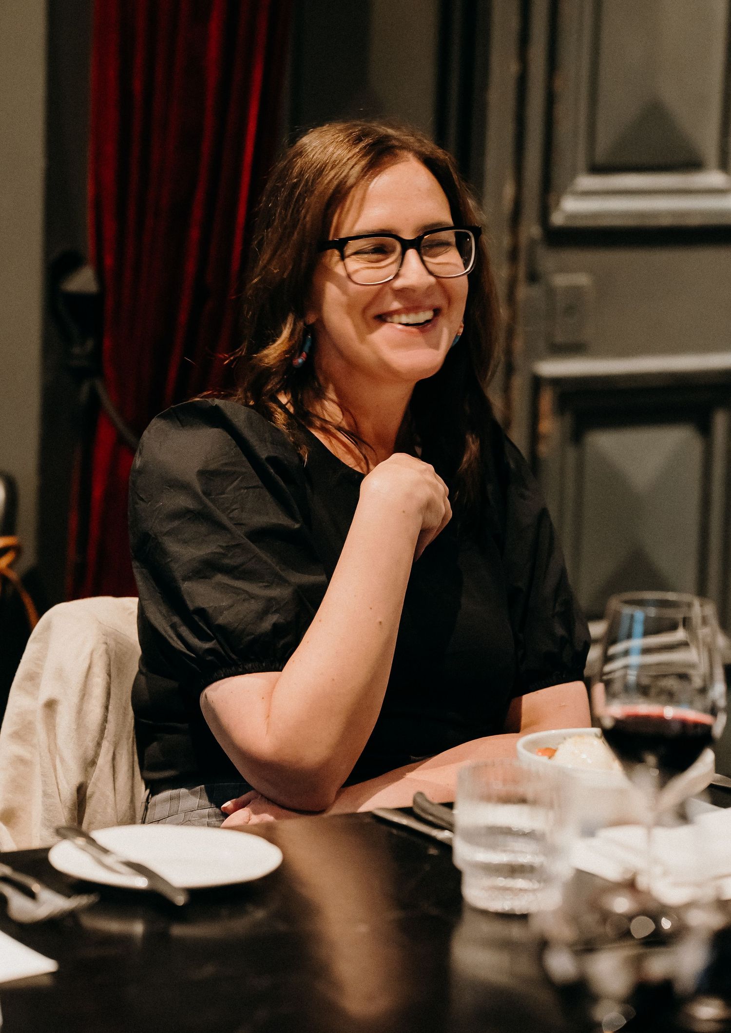 A sequence of four candid photos showing someone laughing and smiling at a dinner table with glasses and plates.