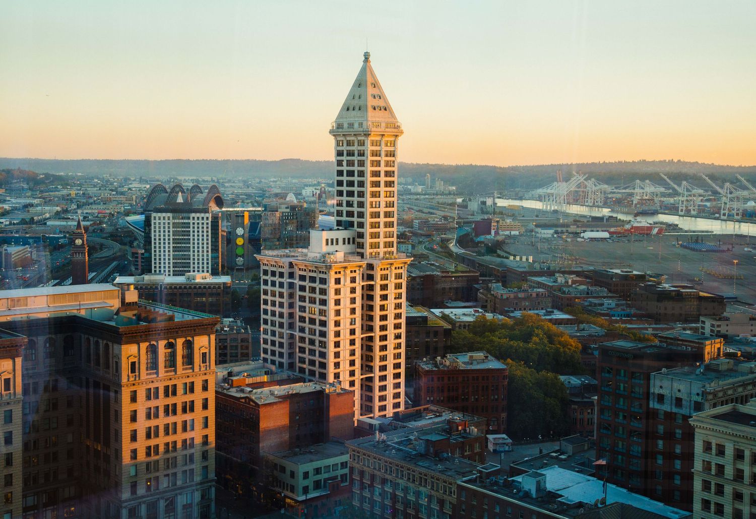 Panoramic cityscape view of downtown Seattle buildings and waterfront during sunset with warm golden lighting.