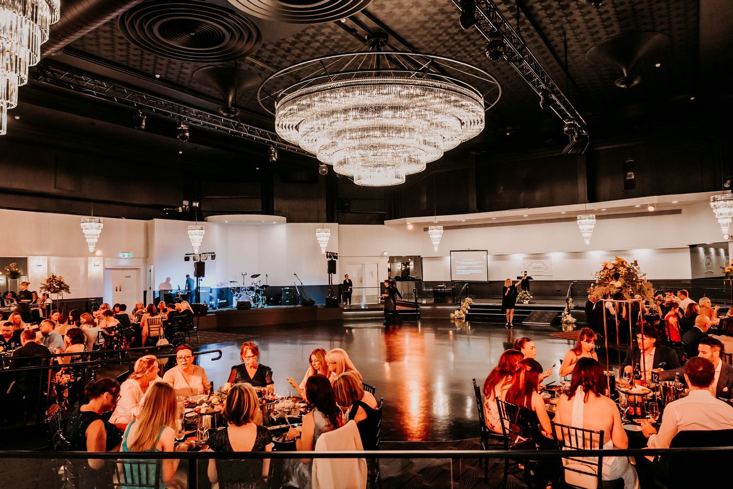 Wedding reception guests dancing on a dimly lit dance floor under a grand crystal chandelier in an elegant ballroom.