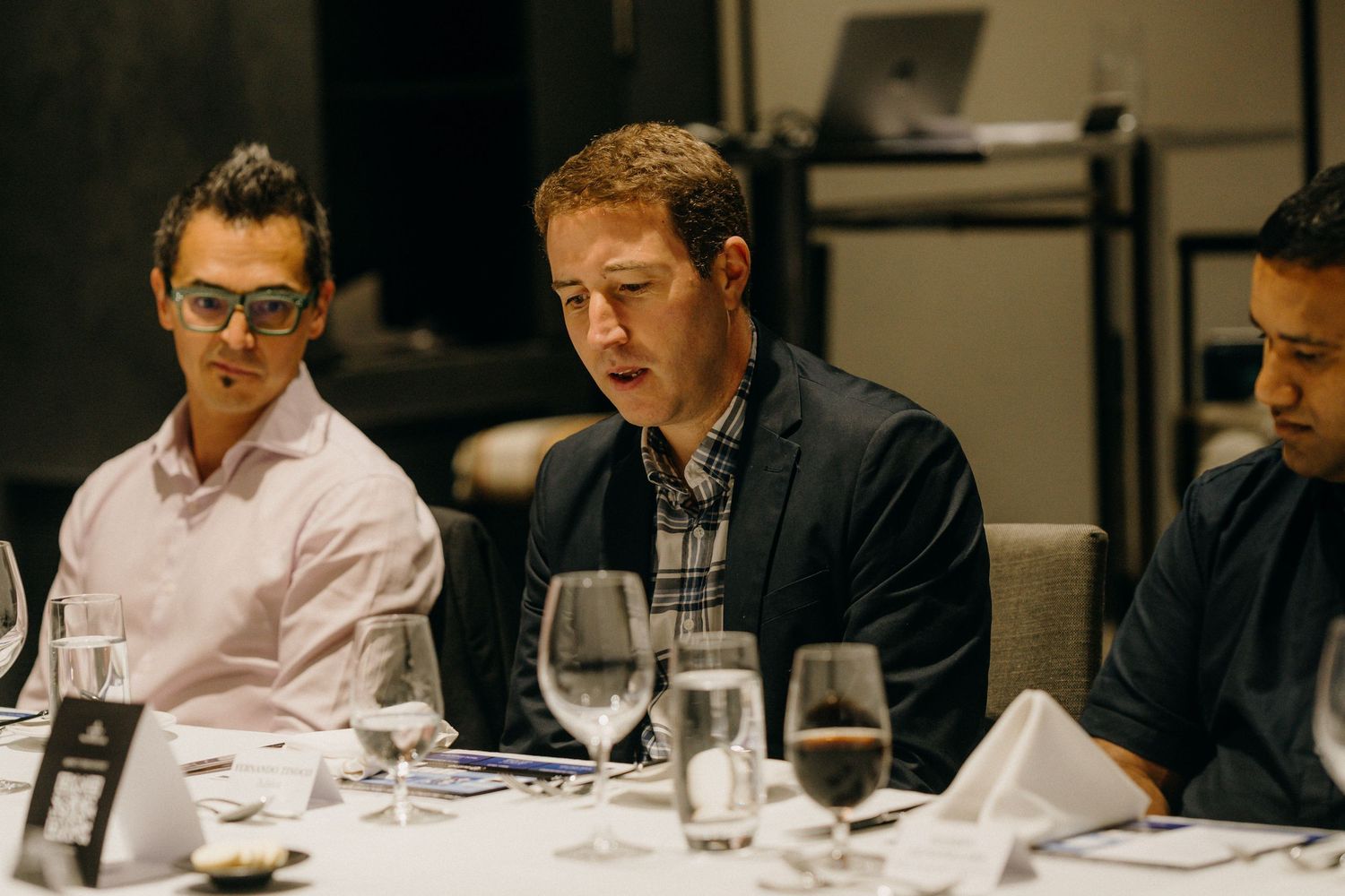 Three businessmen seated at a formal dinner table with wine glasses during a corporate dining event.