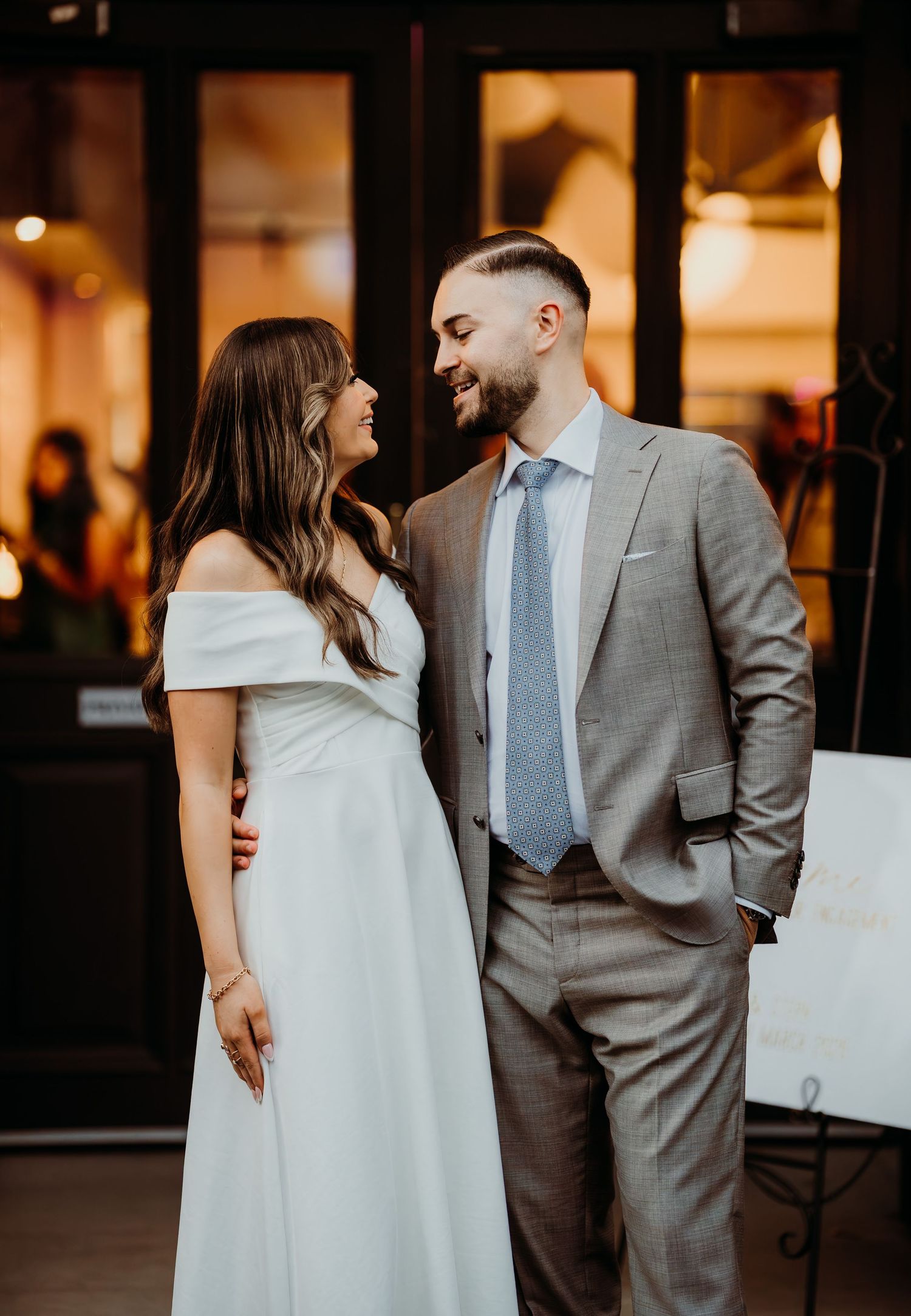 A couple in wedding attire shares intimate moments in six progressive candid shots at a dimly lit indoor venue.