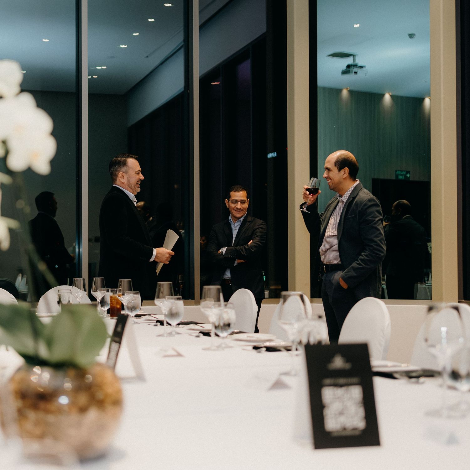 Business professionals having a conversation in an elegant dining room with formal table settings and mood lighting.